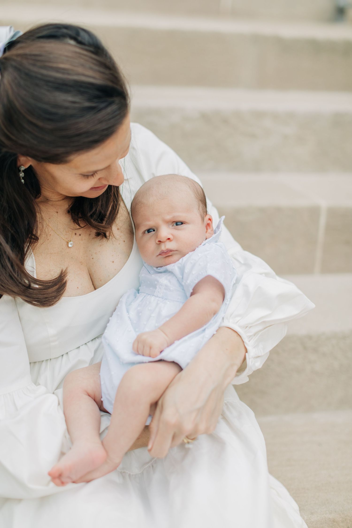 Mother in white dress cradles newborn baby on stone steps.