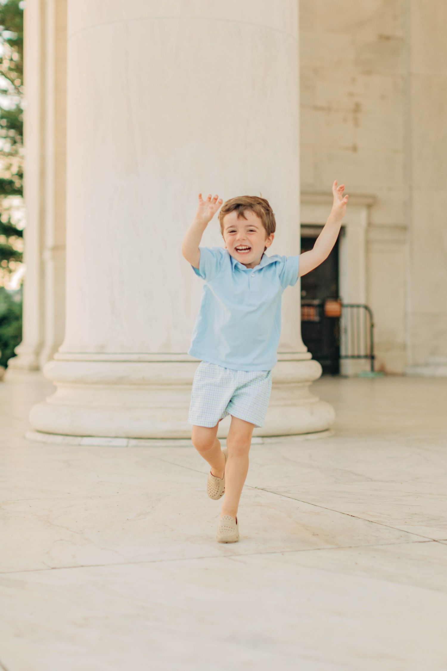Child in light blue outfit running and playing in white columned building.