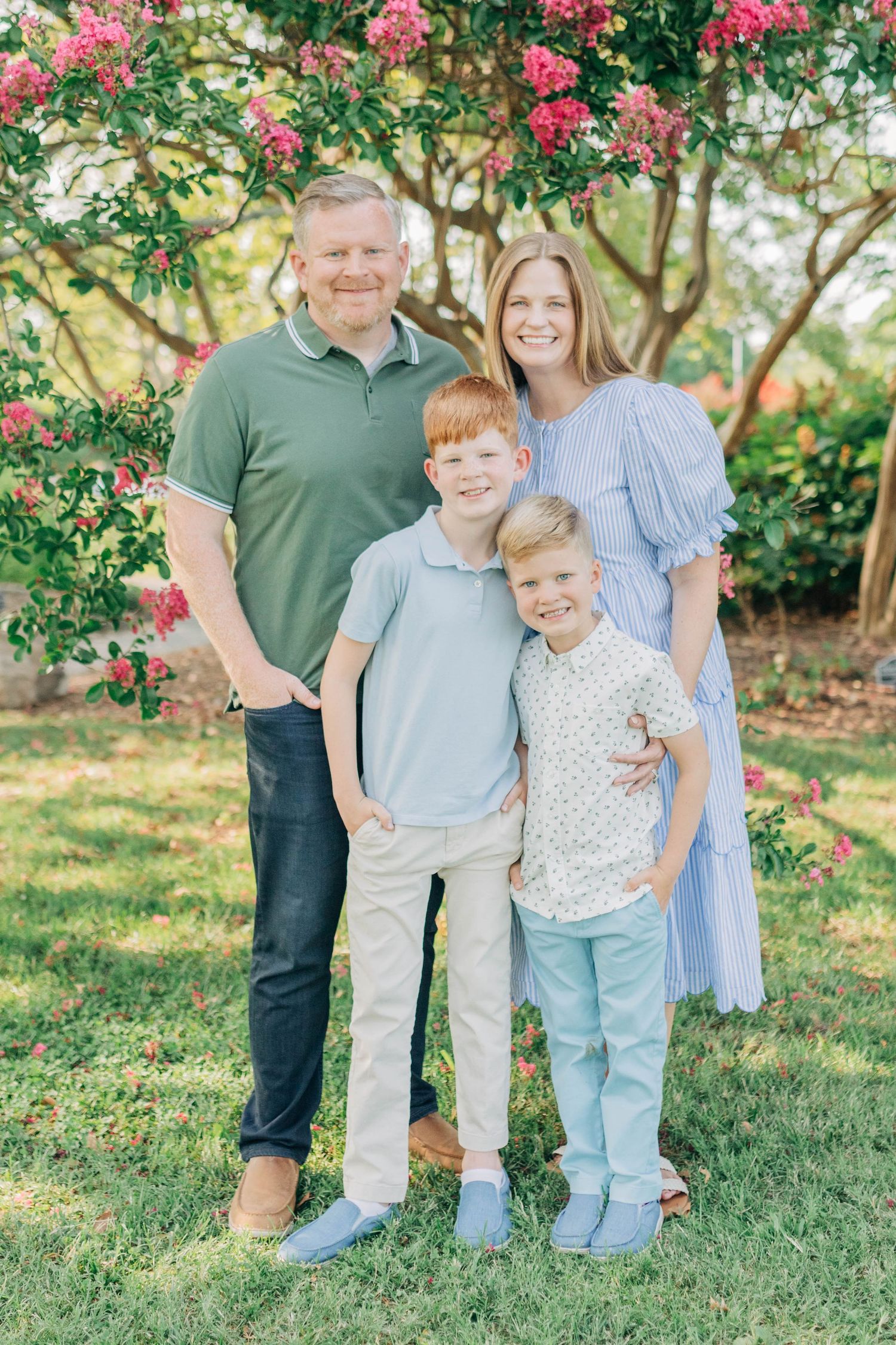 Family portrait with casual poses against a backdrop of pink flowering trees and green foliage.