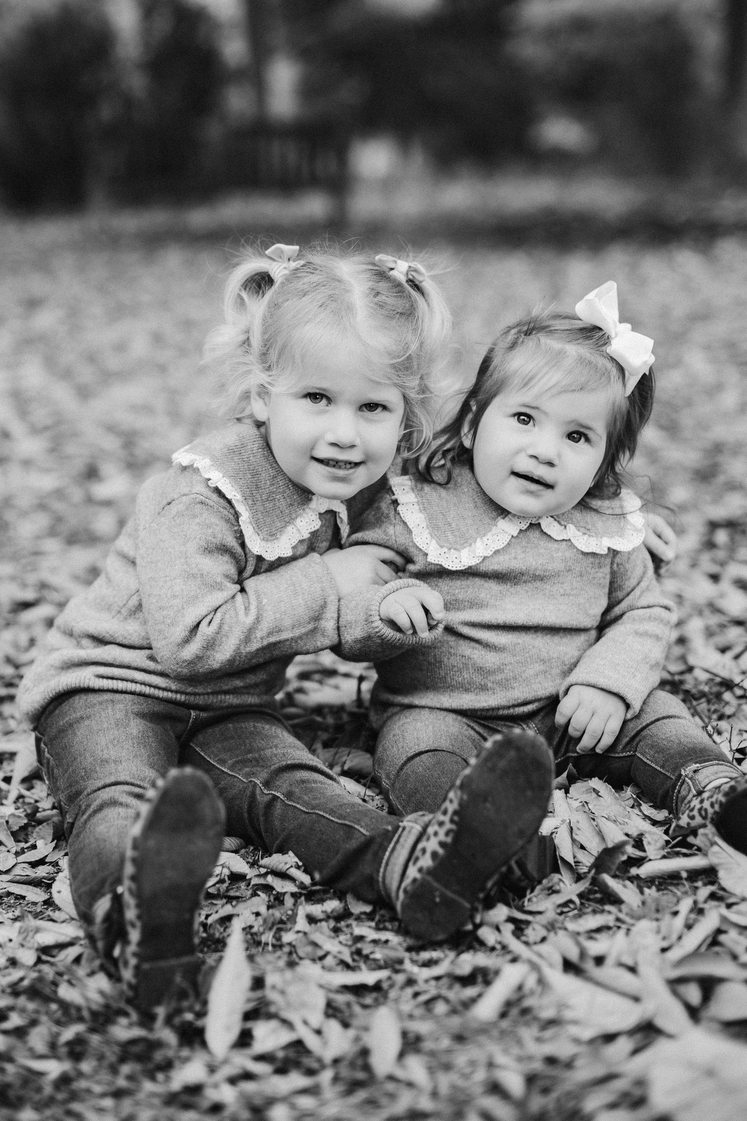 Two children sitting together on fallen autumn leaves in black and white photography.