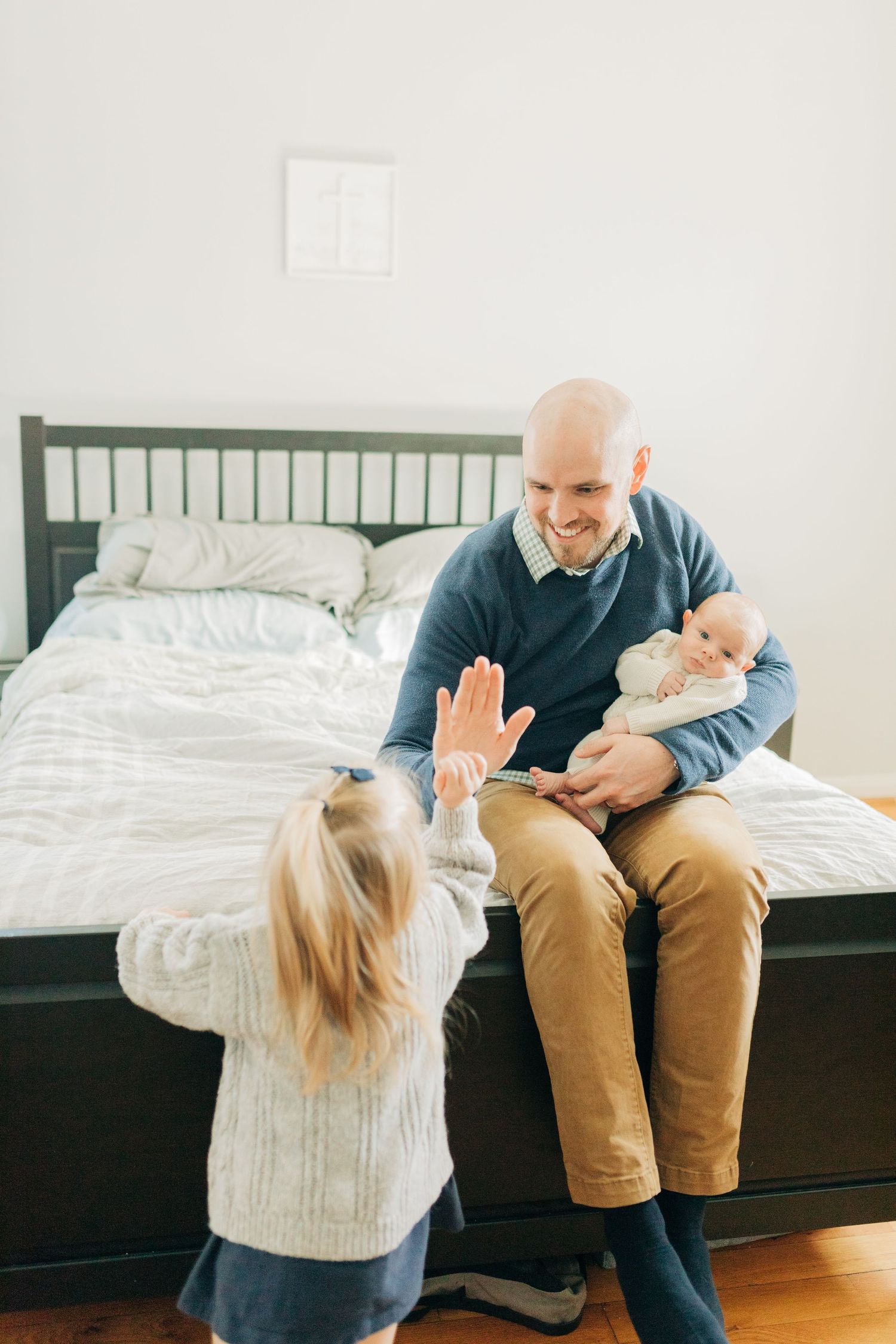 Playful interaction between family members sitting on dark furniture against white walls.