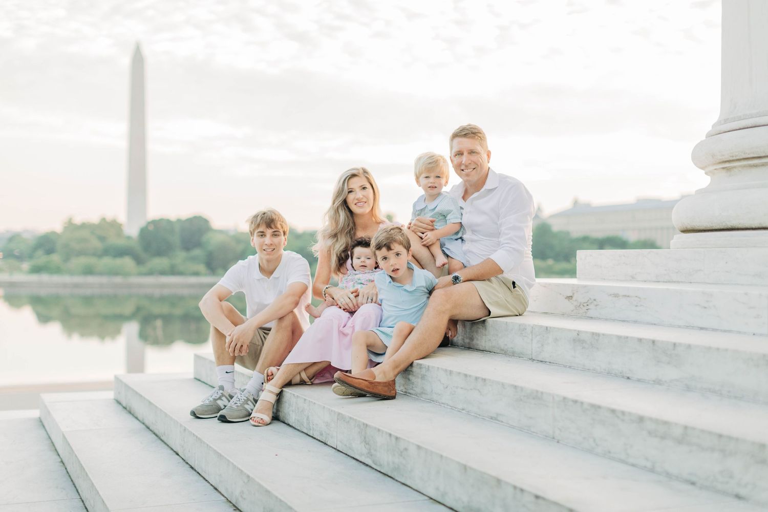 Family relaxing together on outdoor stone steps near water.