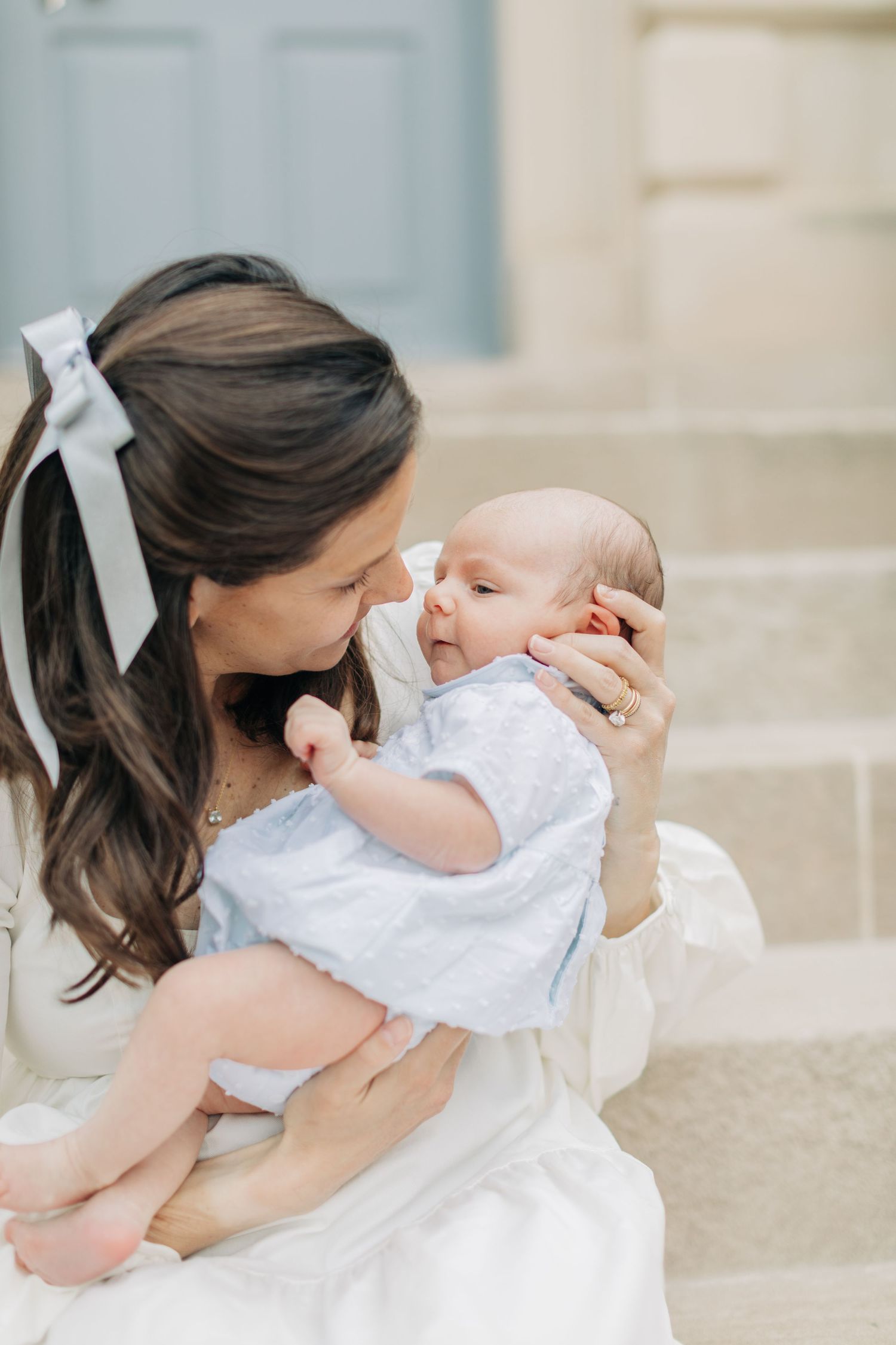 Mother in white dress lovingly holds infant on outdoor stone steps.