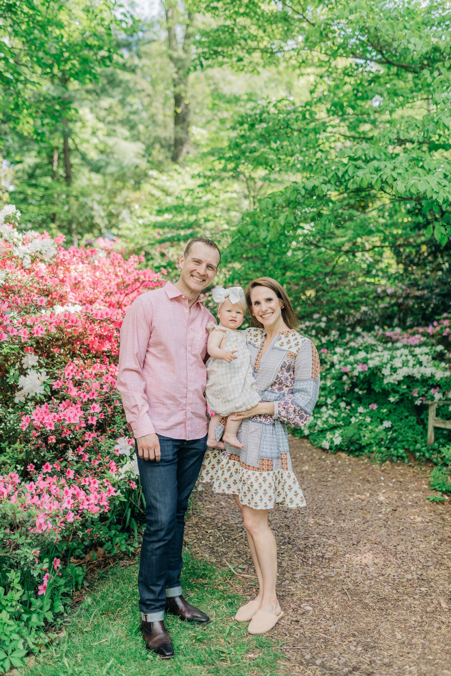 Family portrait in garden path with blooming pink azaleas and green foliage.
