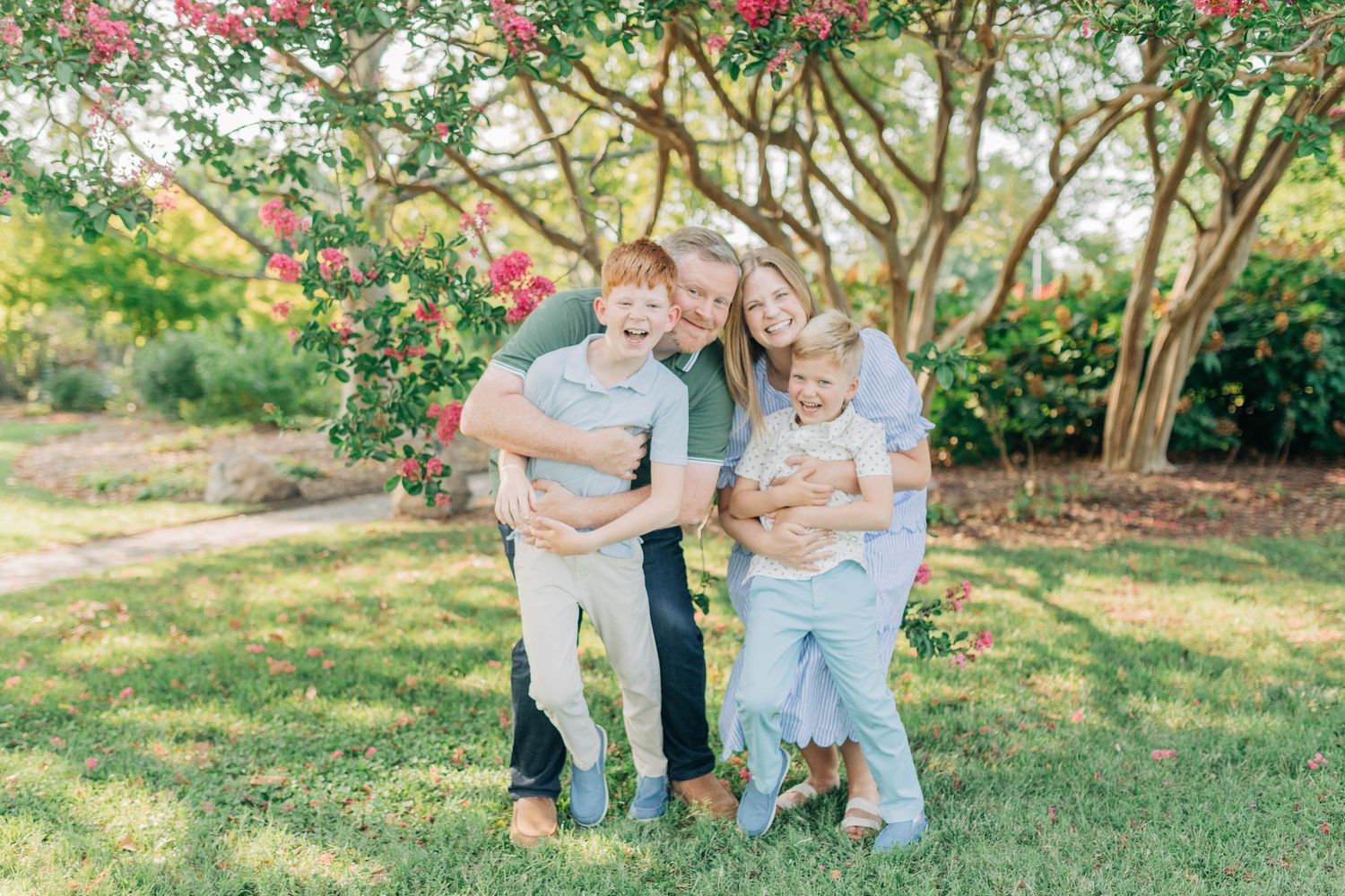 Family portrait session in a garden with blooming pink flowers and lush greenery.