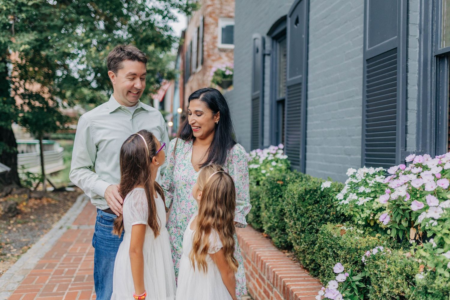 A happy family of four with two young girls walks along a brick path beside blooming hydrangeas.