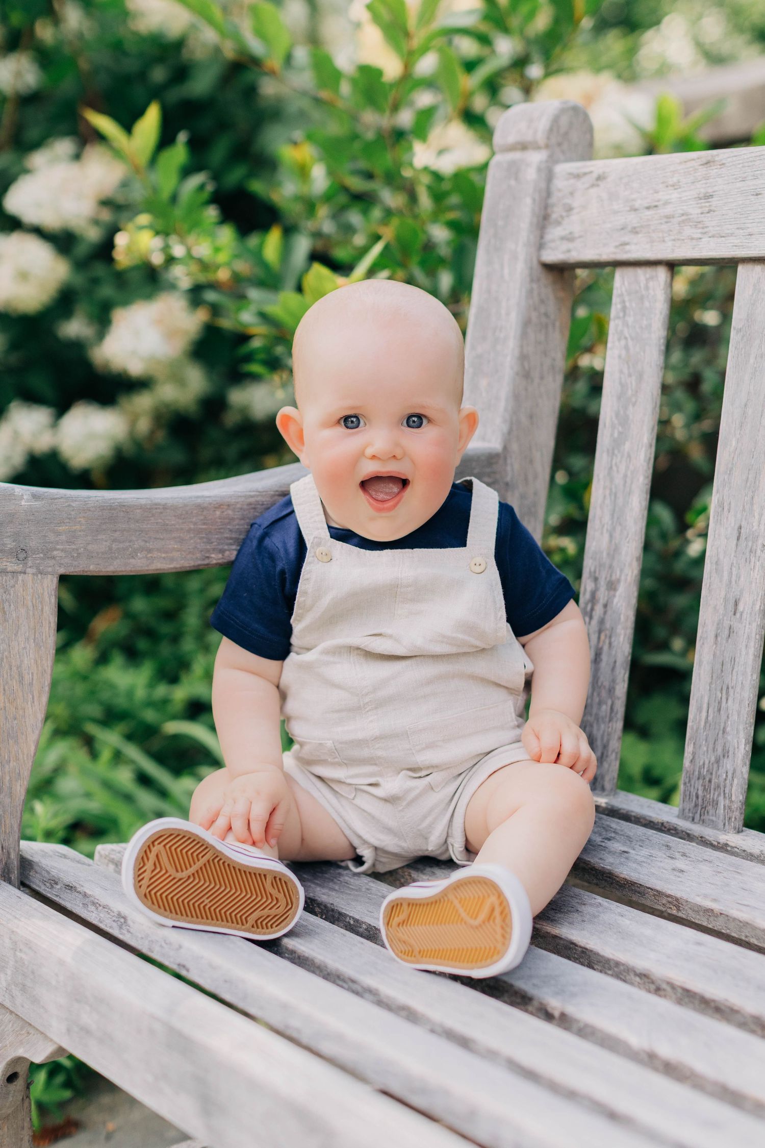 Adorable smiling baby sitting on a wooden bench in a sunny garden.