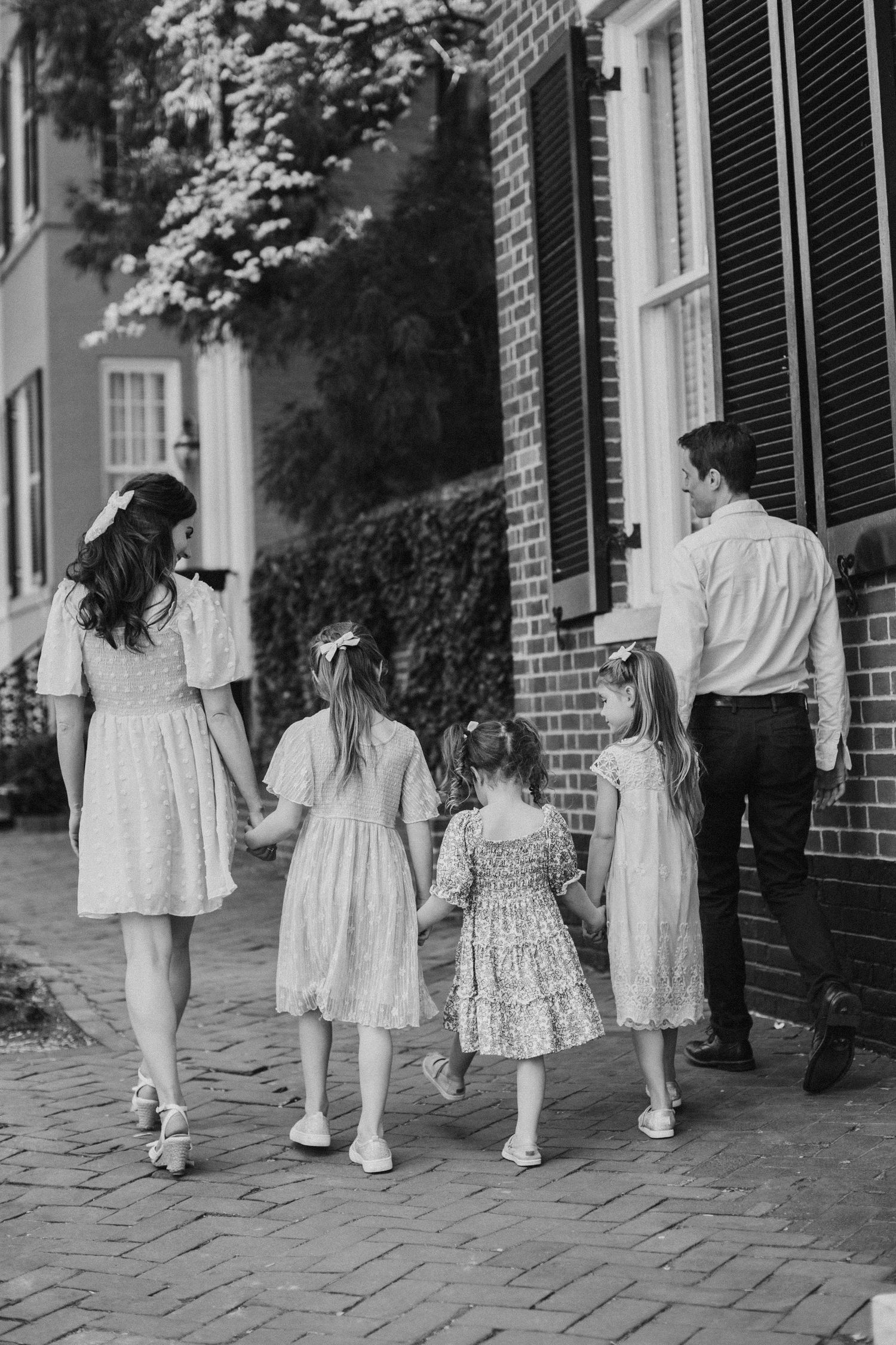 Black and white photo of a family of five walking hand-in-hand along a historic brick sidewalk in spring.
