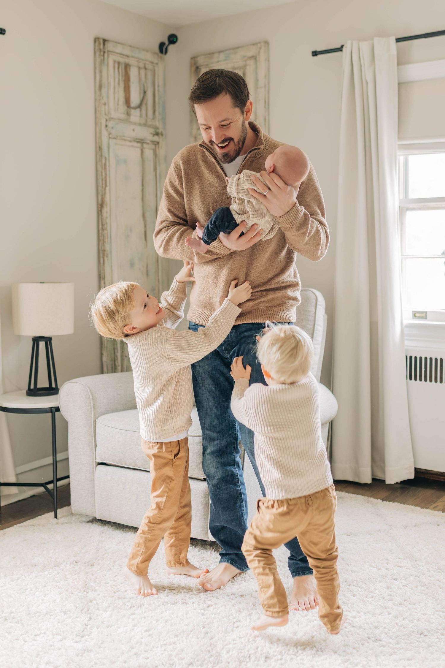 Playful interaction between parent and children on a white carpet in a bright room.