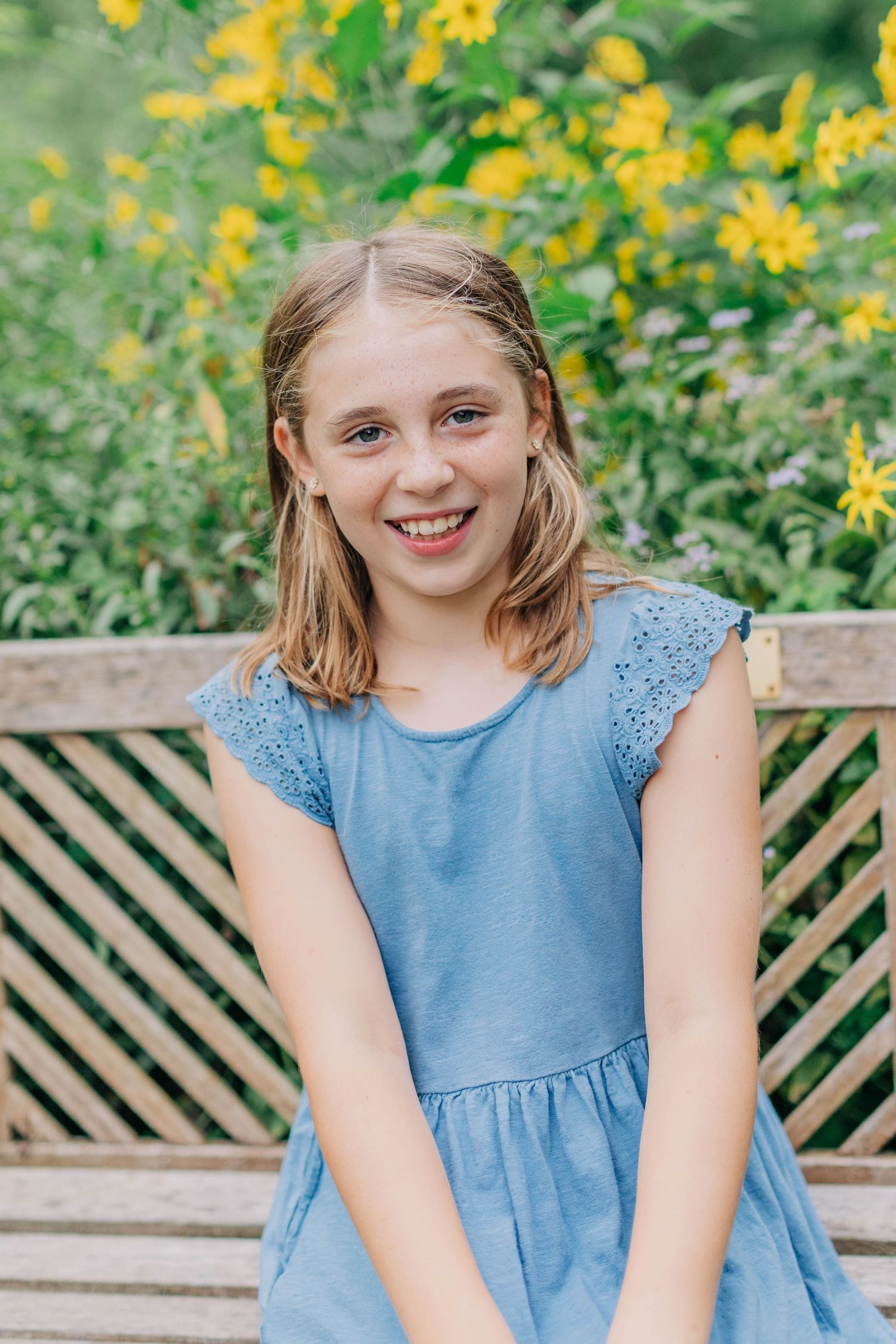 Portrait session in a garden with yellow flowers and a lattice fence in the background.