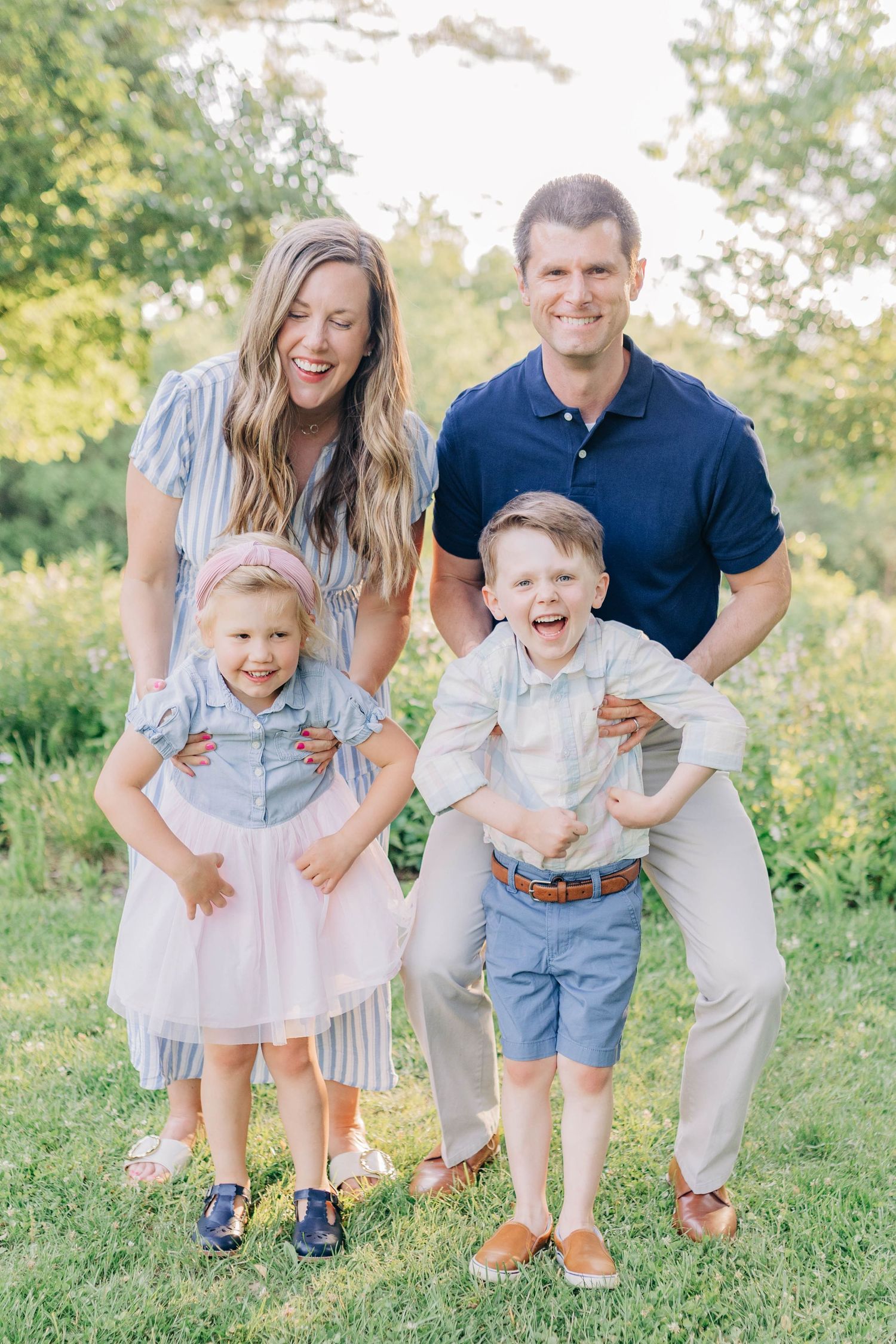 A family plays and laughs together on a grassy hillside during a summer photoshoot.