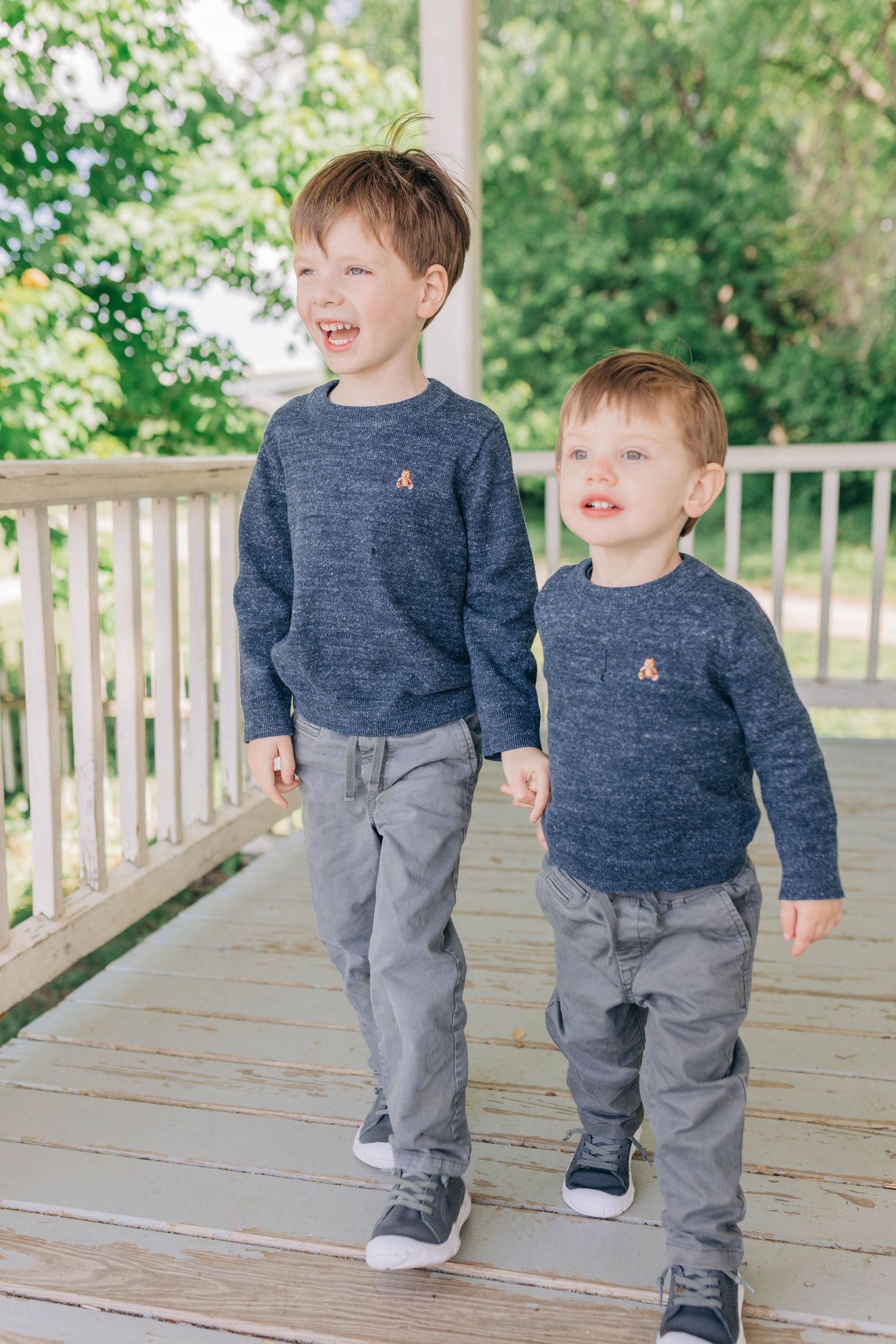 Two children in matching navy sweaters and gray pants playing on a wooden deck.