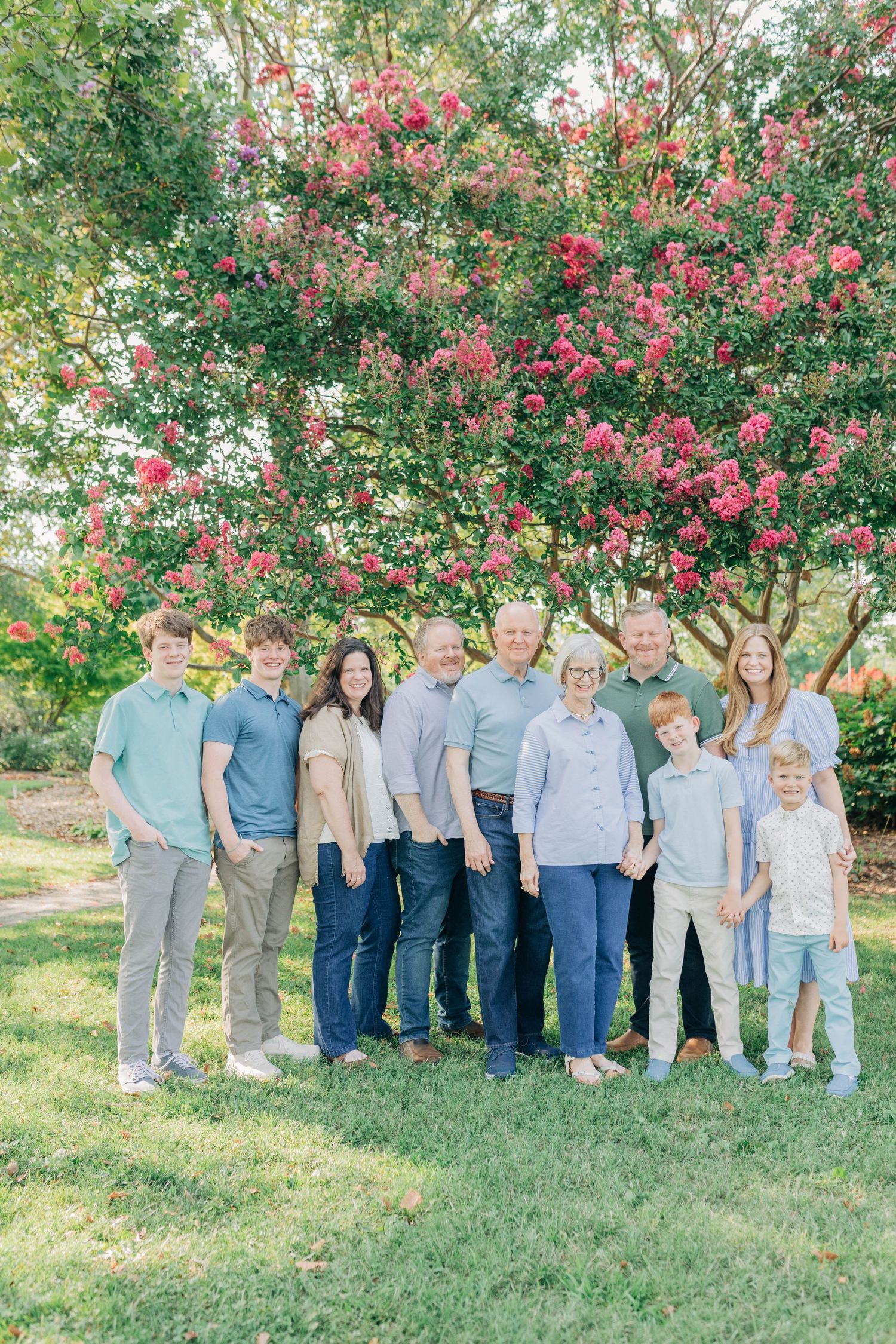 Extended family group photo with everyone wearing coordinated blue and grey outfits in a garden setting.