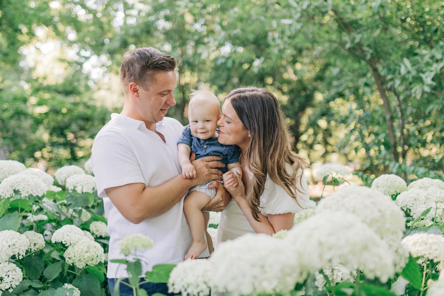 Beautiful outdoor family photoshoot among blooming white hydrangea bushes.