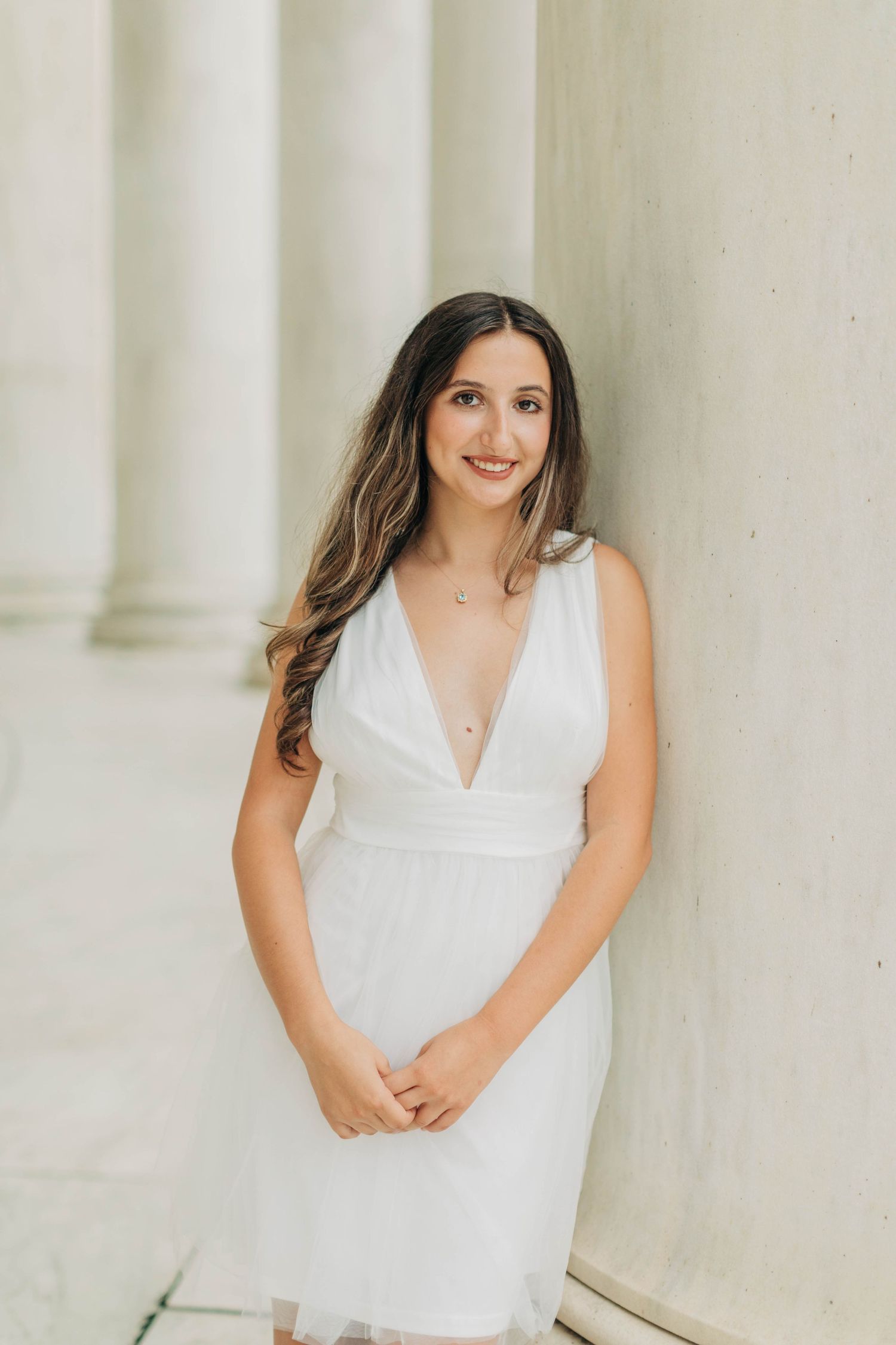 Portrait in white dress against classical marble columns with soft natural lighting.