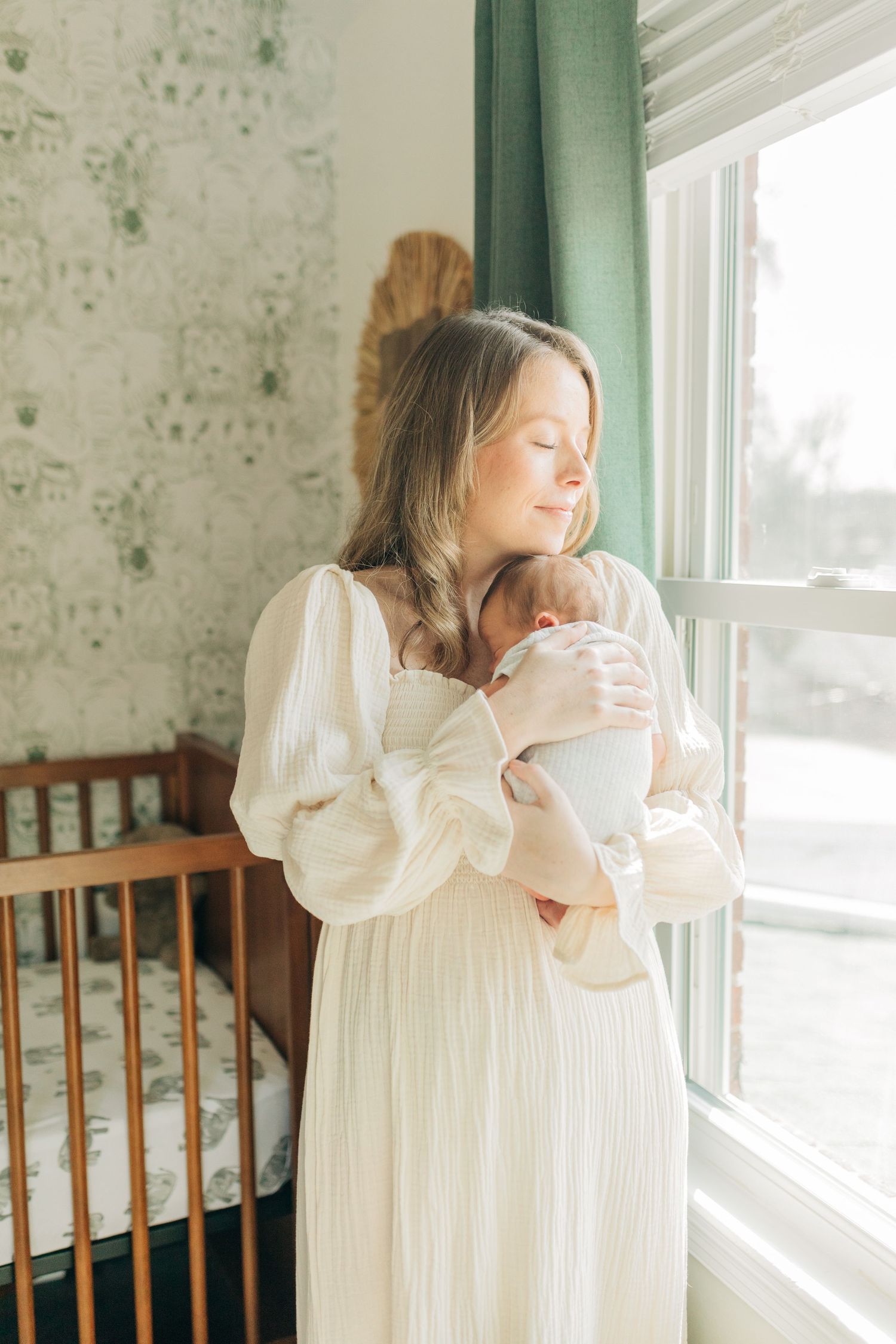 Peaceful moment in nursery with soft natural light and green curtains.