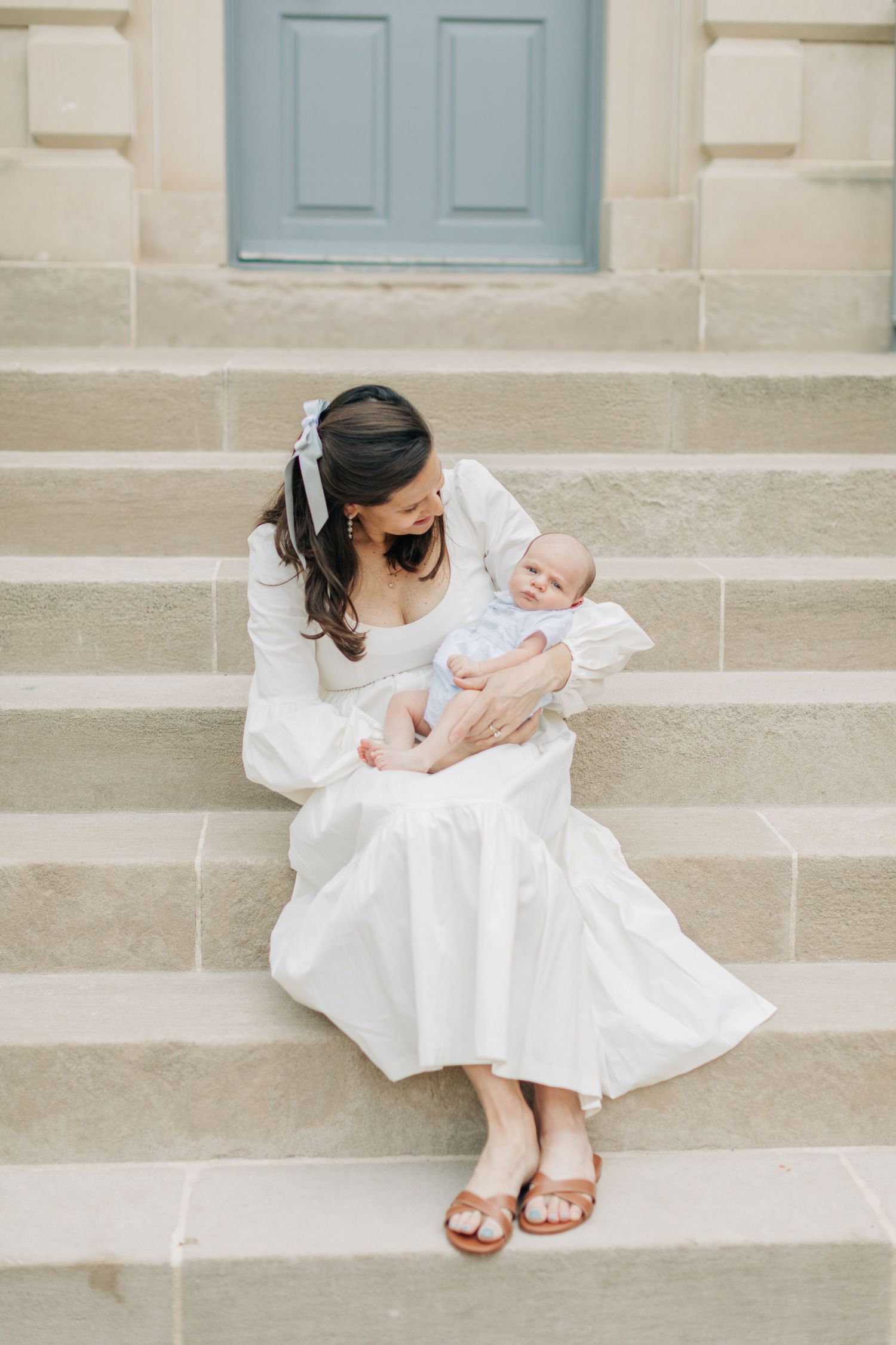 Mother in white dress sits on stone steps holding baby in tender moment.
