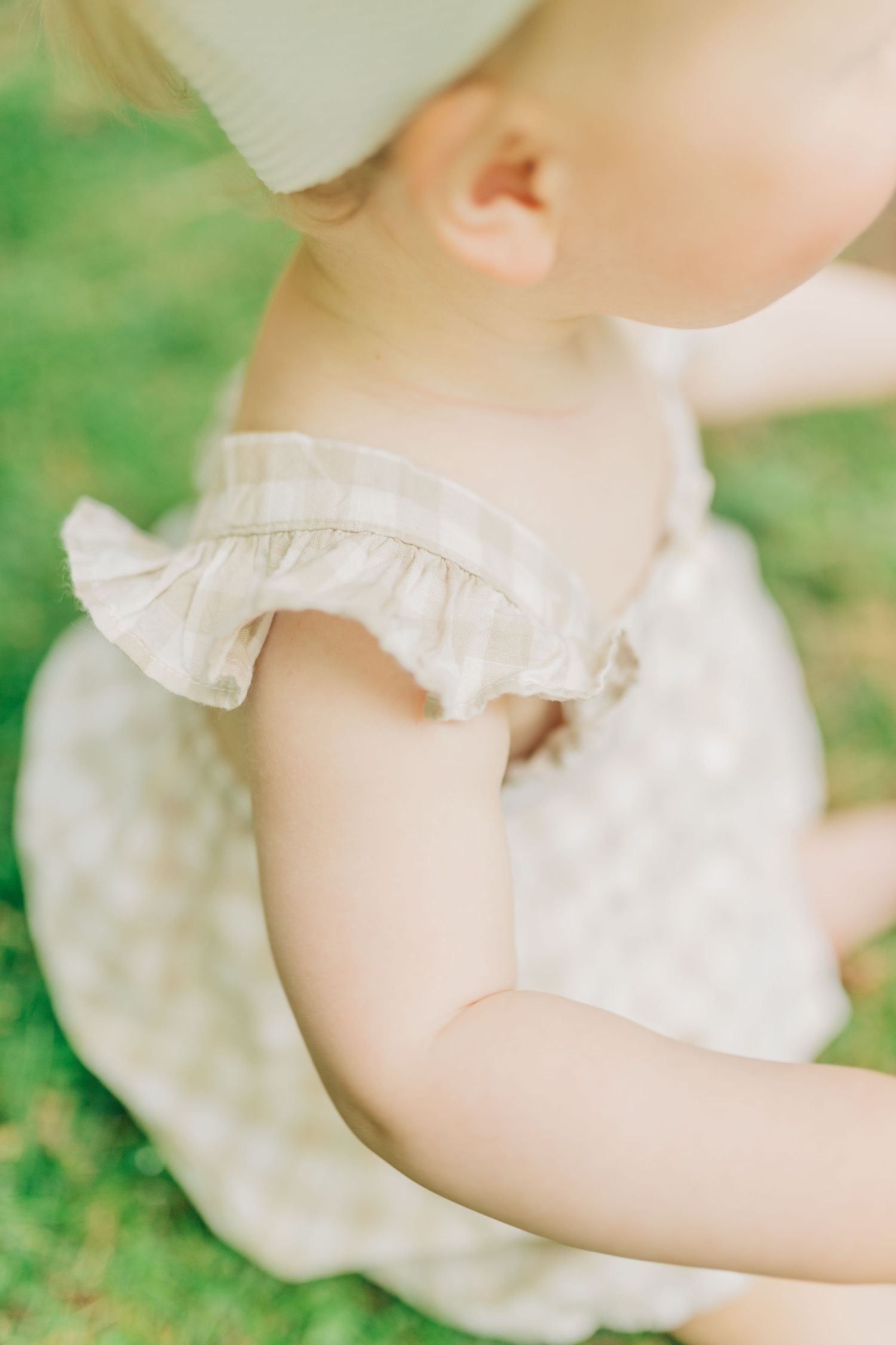 Close-up detail of a ruffled sleeve on a light-colored linen dress against a green background.