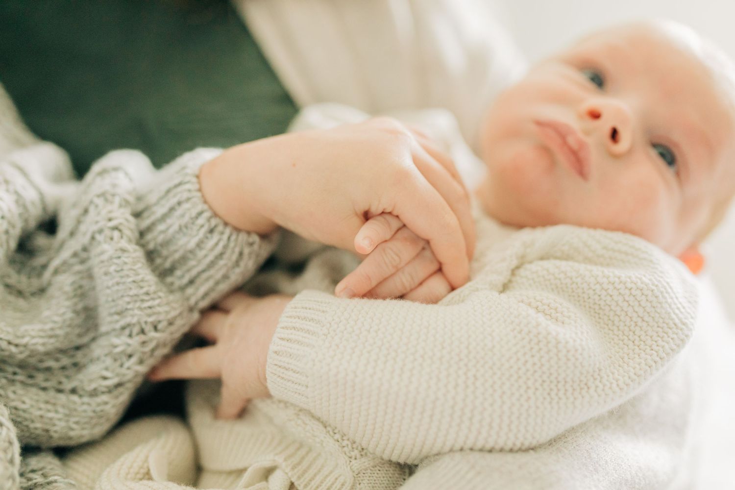 Close-up of tiny baby hand and knit sweater detail during tender moment.