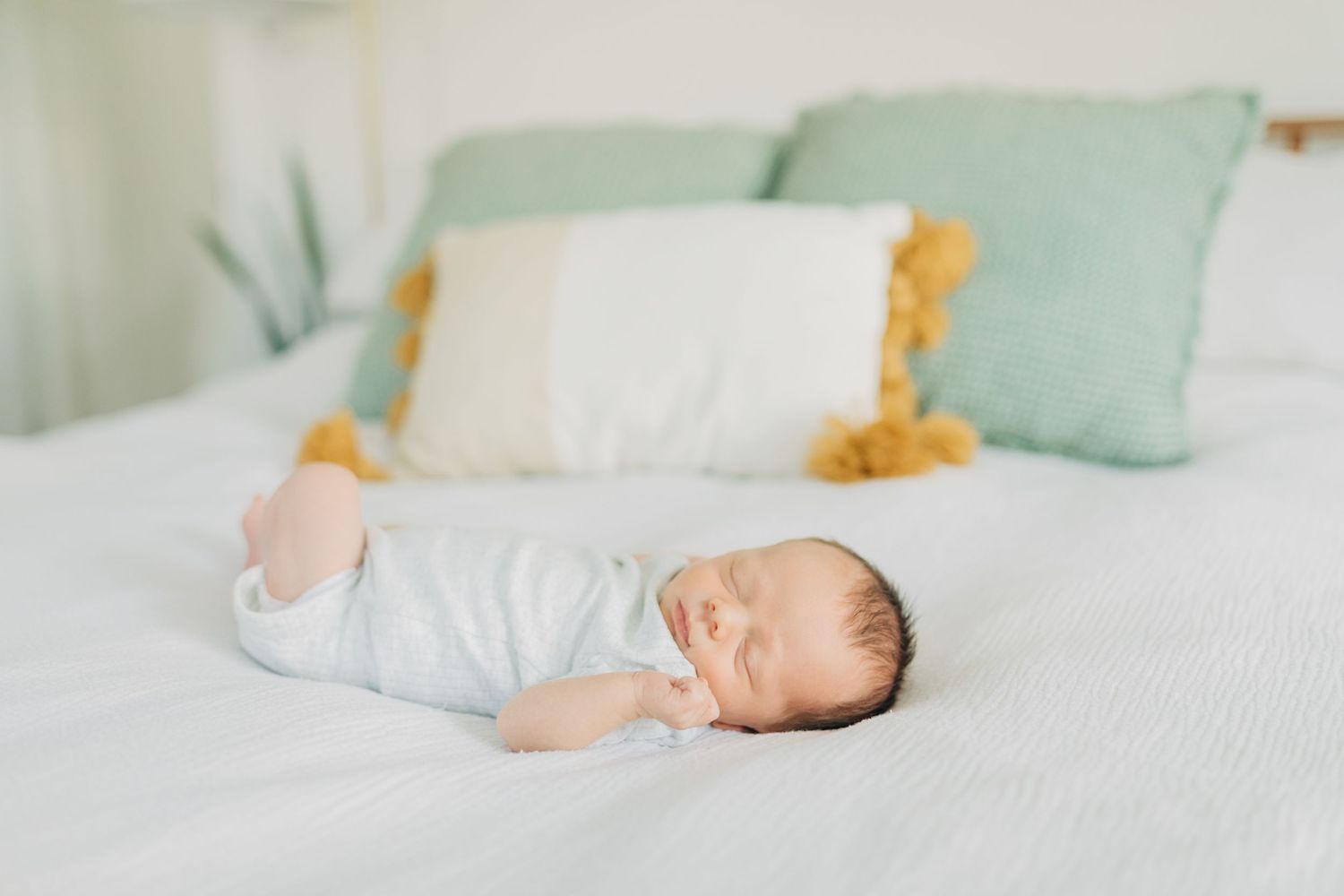 Peaceful sleeping newborn on white bedding with soft mint green decor and stuffed giraffe.