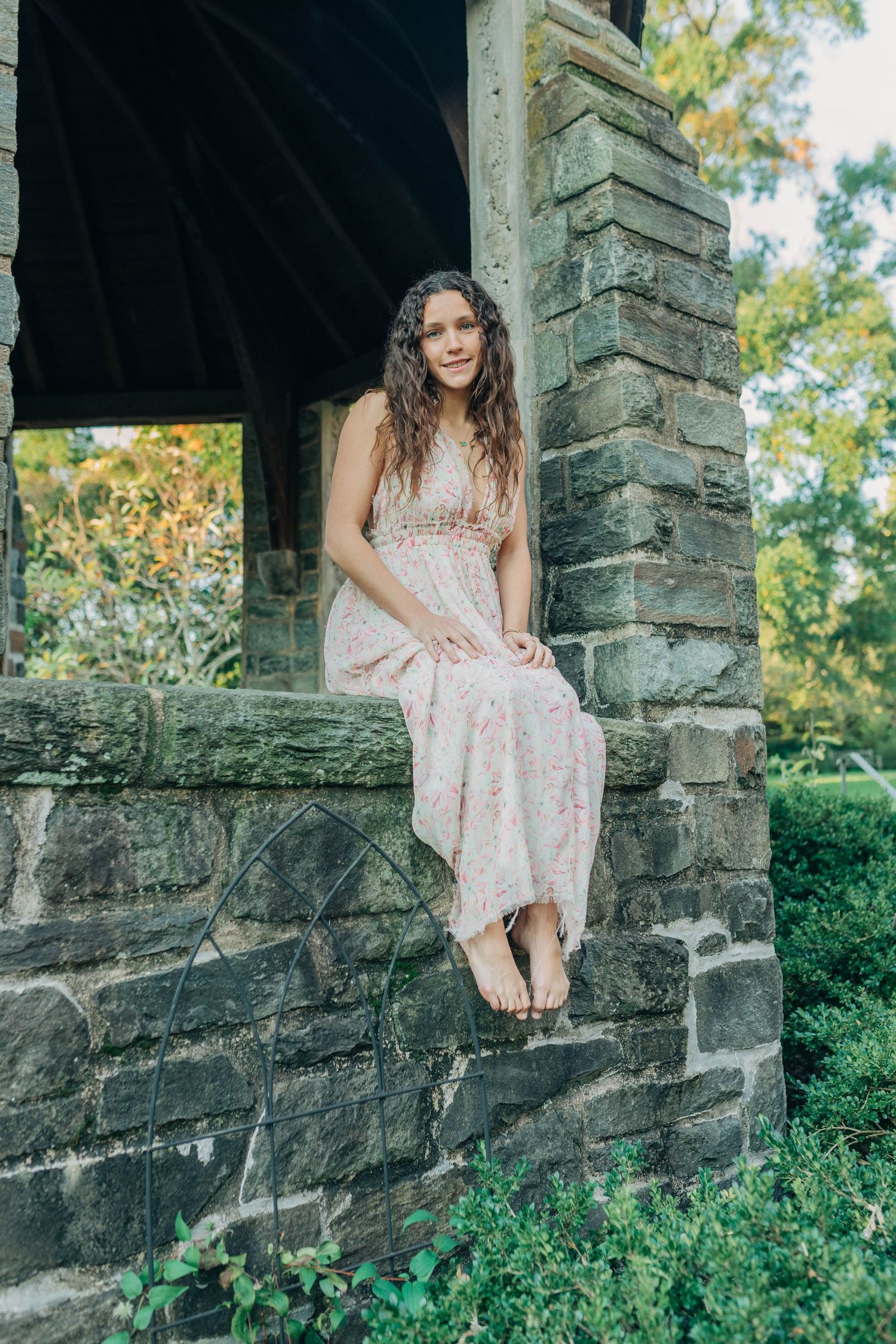 Stone wall and lush greenery create a rustic backdrop for outdoor portrait photography.
