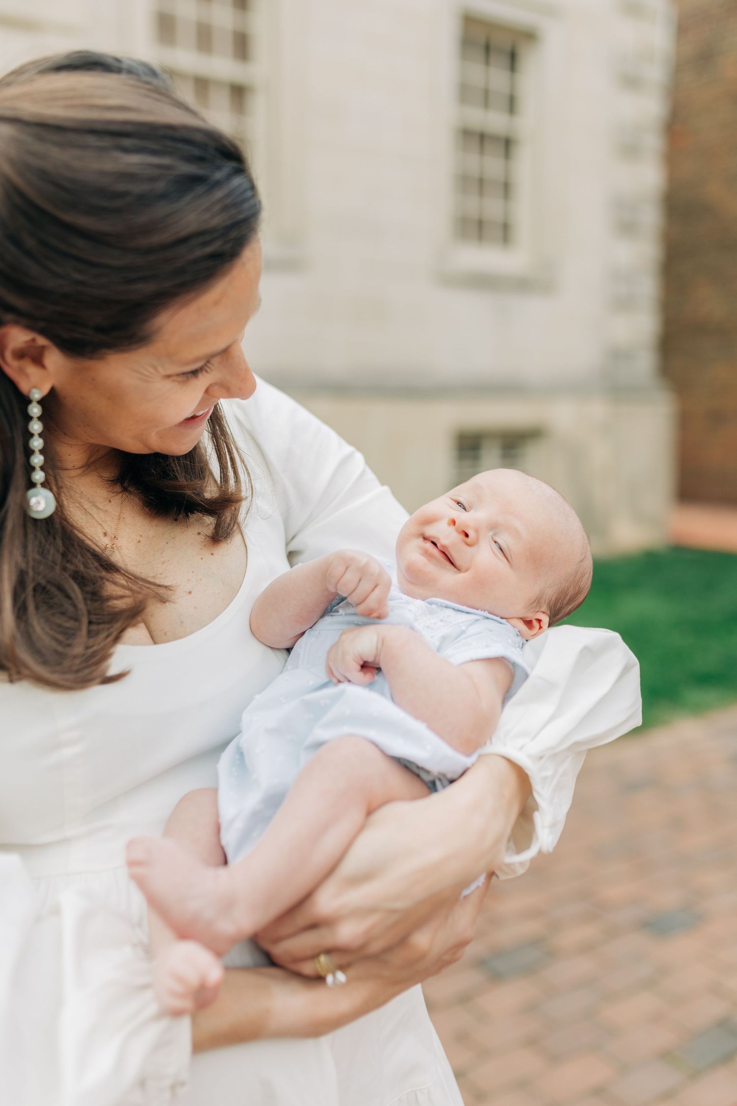 Woman in white dress tenderly holding and gazing at a sleeping infant.