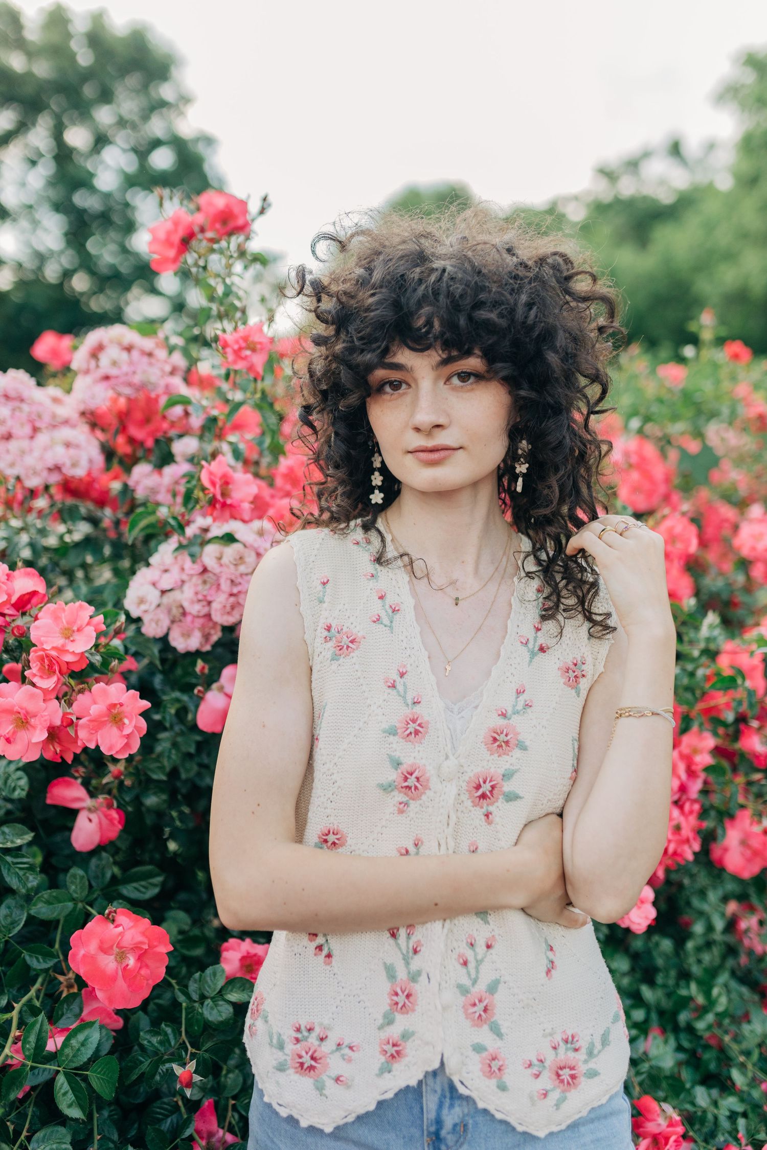Person in floral vest poses confidently against backdrop of pink roses in garden setting.