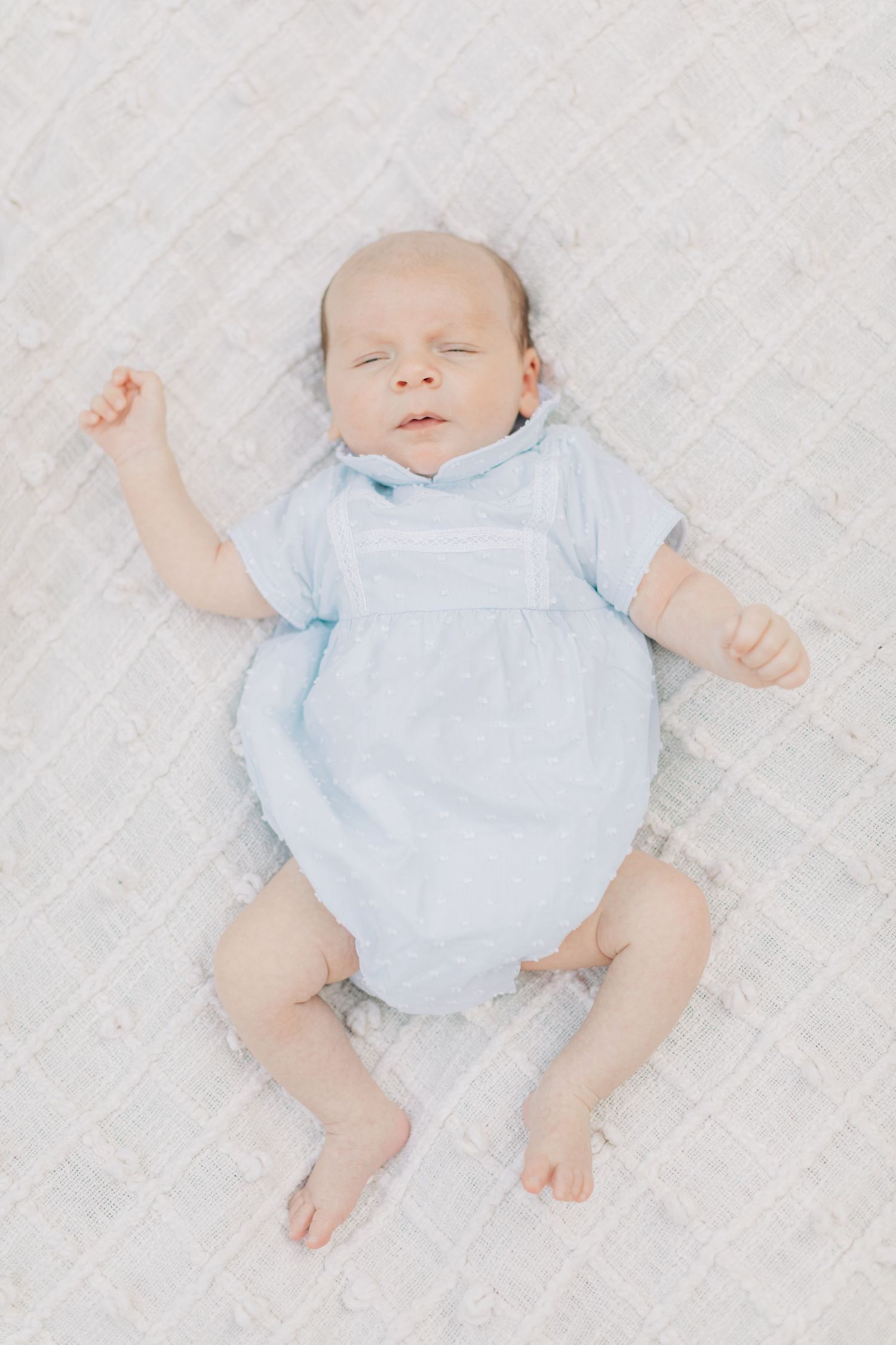 Baby in light blue outfit lying on white textured fabric.