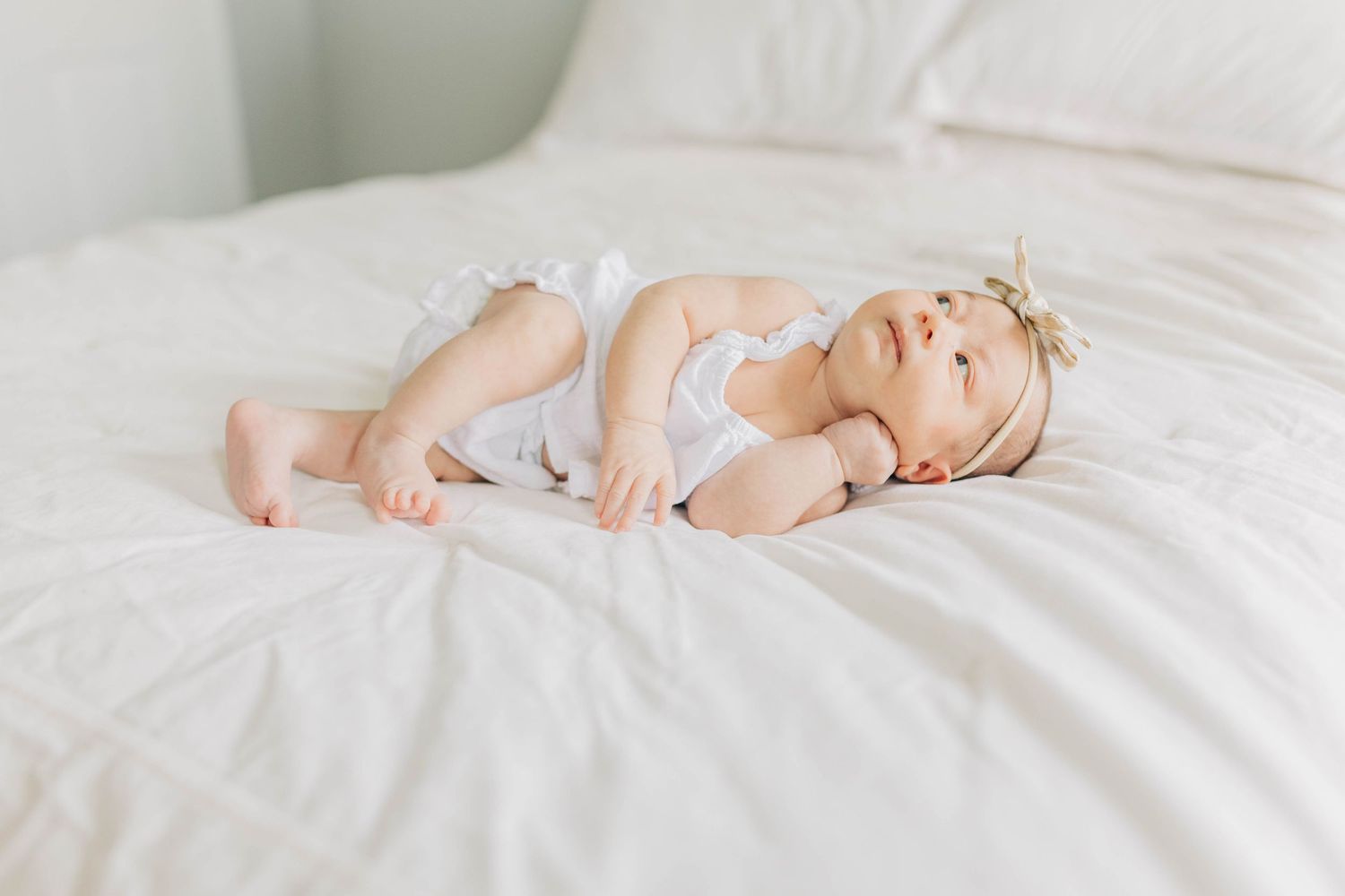 A sleeping infant lies peacefully on white bedding in natural light.