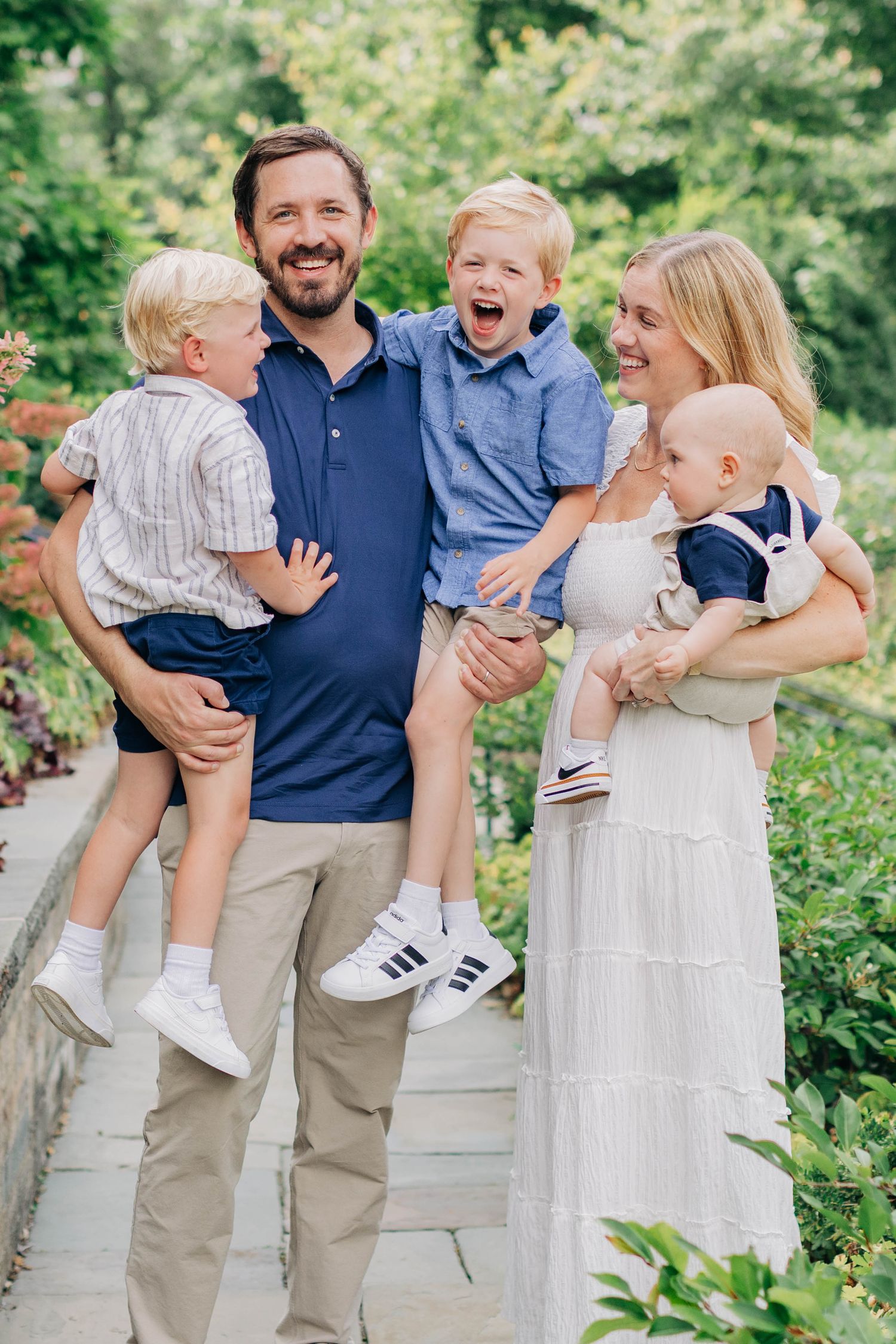 Happy family with three young boys posing outdoors in a lush garden setting.