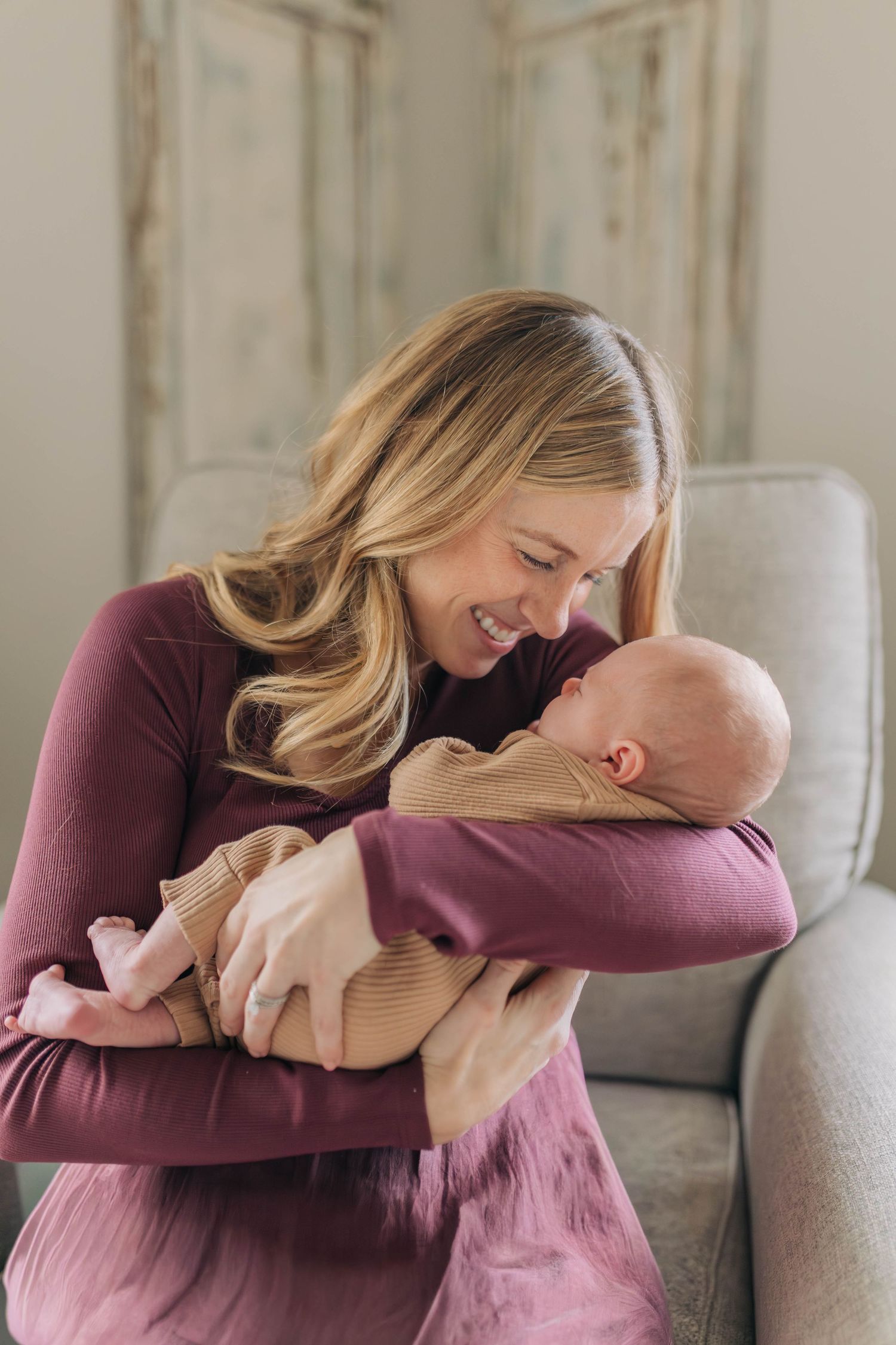 Tender moment between mother in burgundy dress and baby in beige outfit.