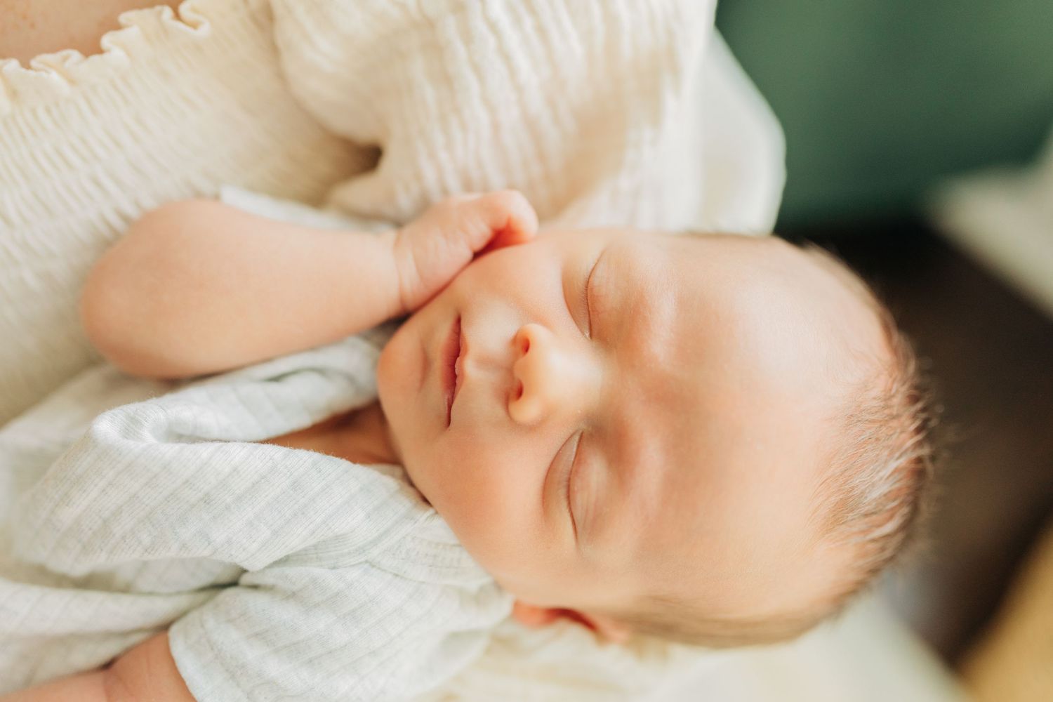 Close-up of sleeping infant with serene expression wearing white clothing.