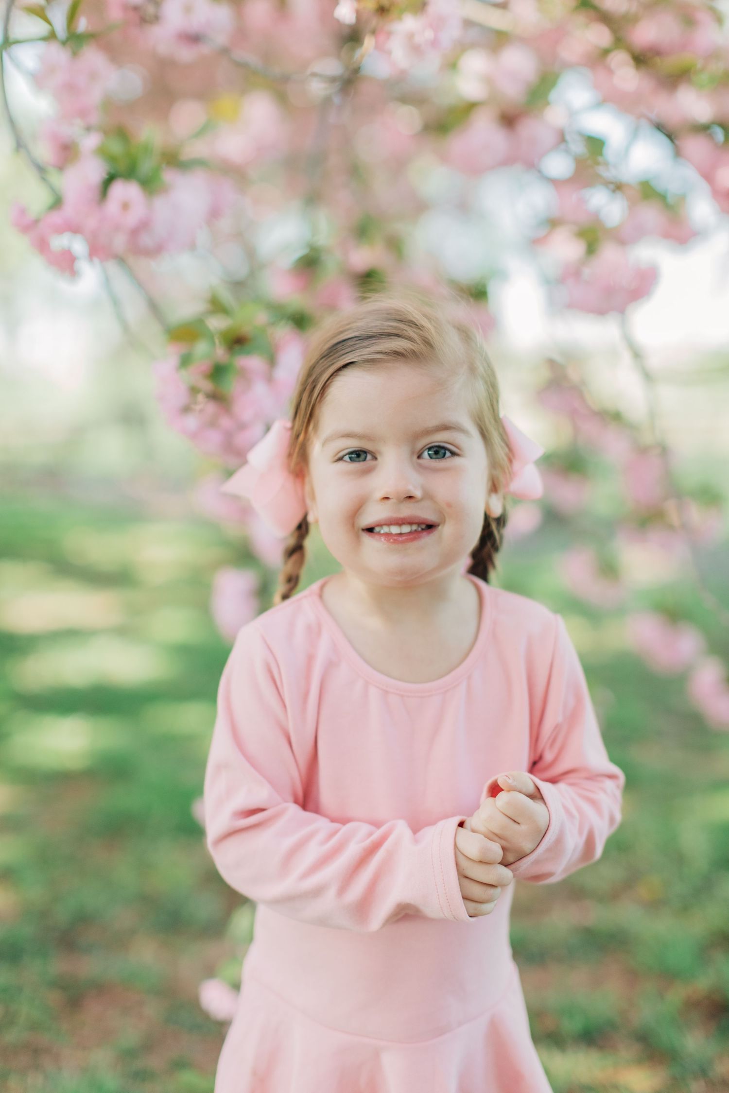Close-up portrait of child in pink dress beneath flowering cherry trees.
