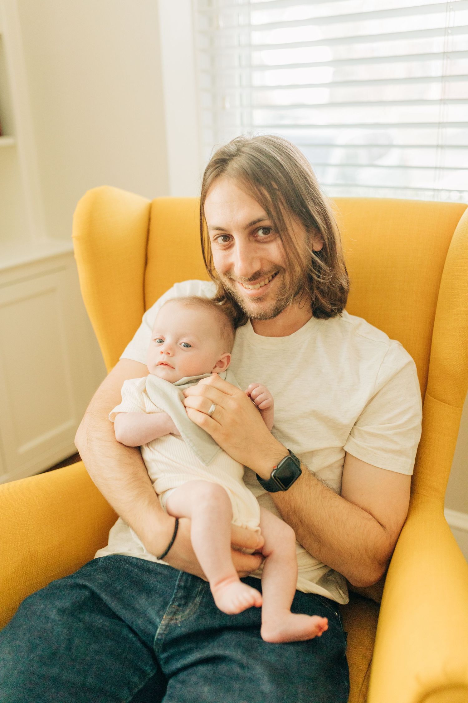 Intimate family moment captured on a mustard yellow armchair in a cozy living space.