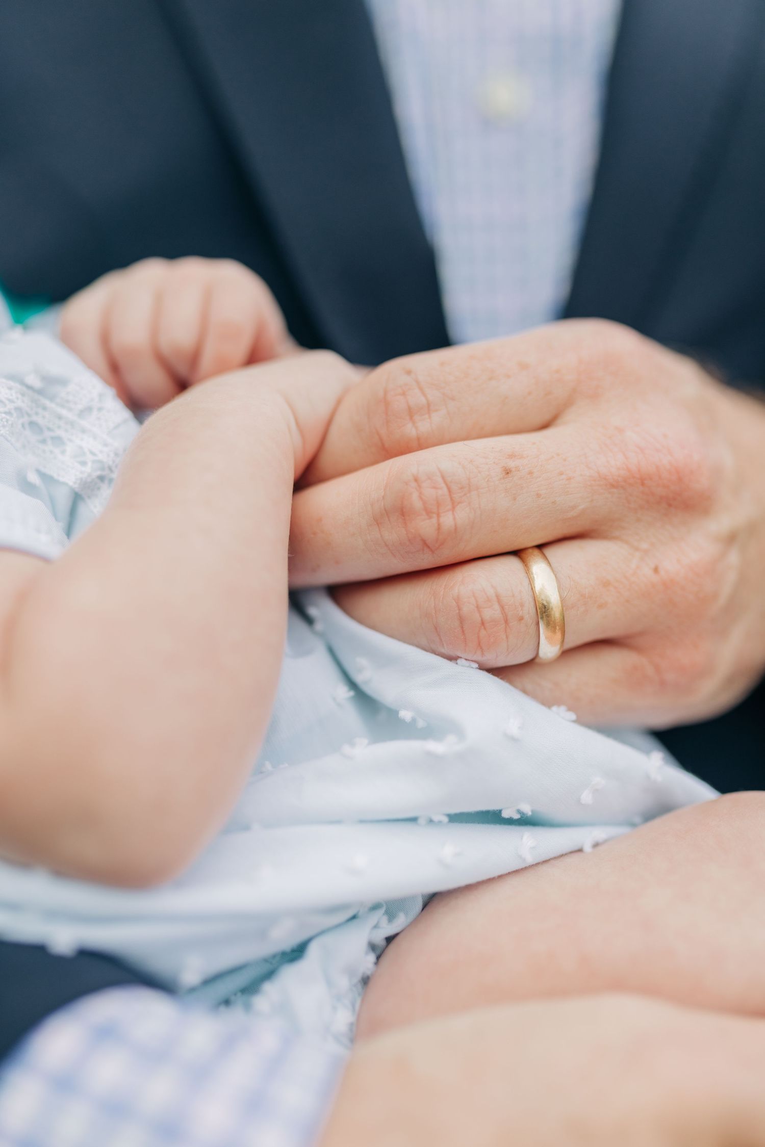 Close-up detail shots of tiny baby hands being gently held, with a gold ring visible.