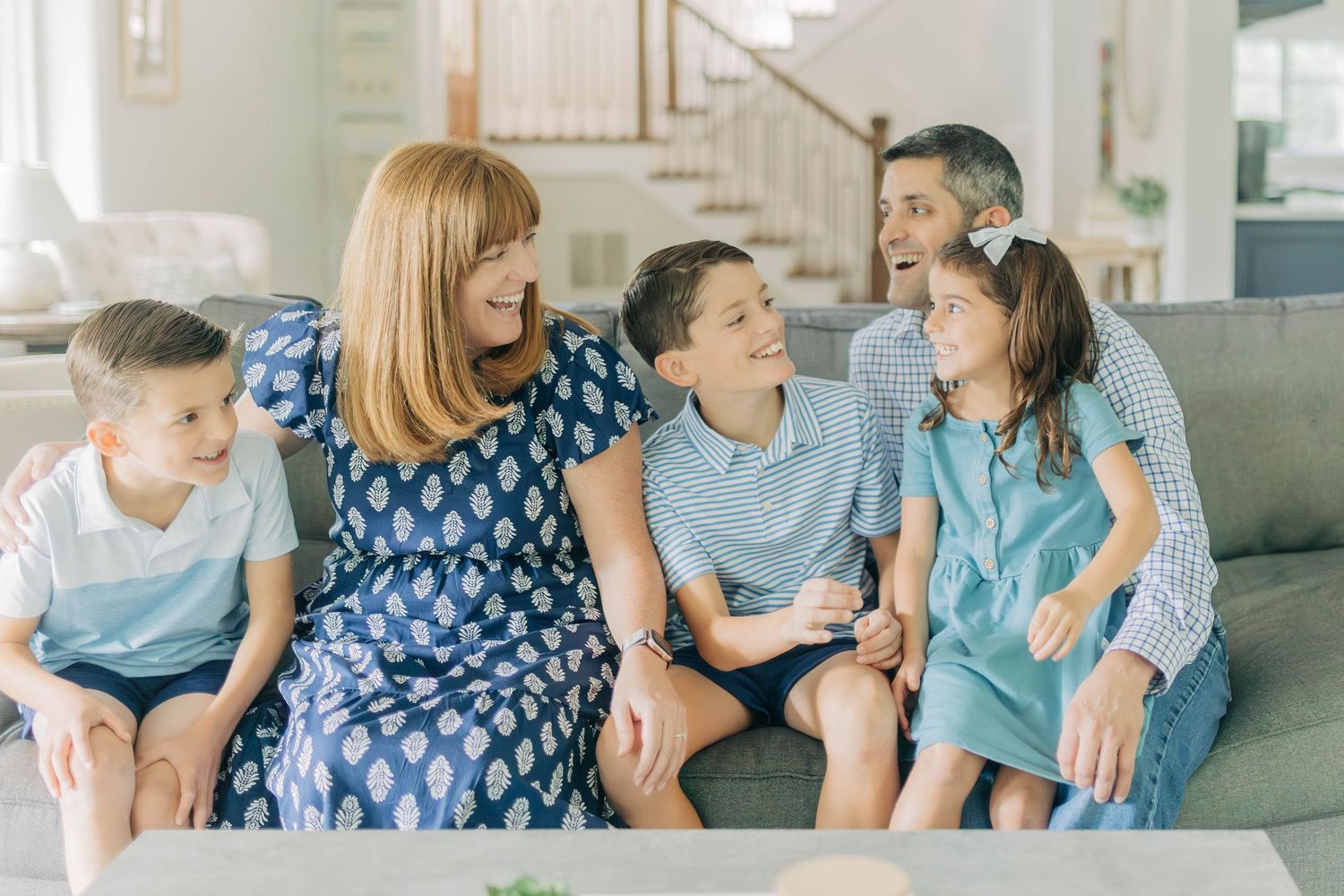 Family relaxes together on gray couch during indoor lifestyle photo session.