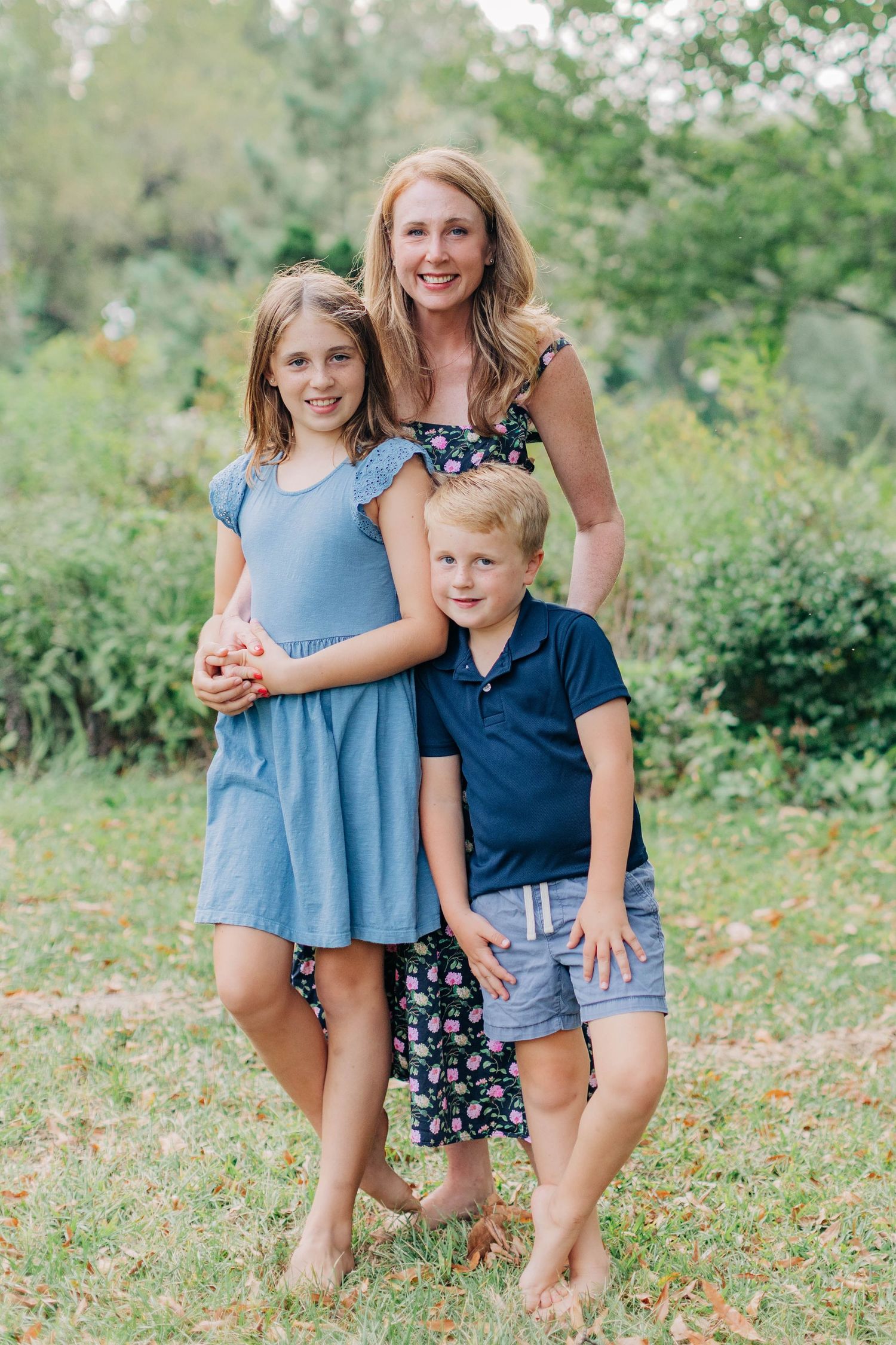 Three people pose together outdoors in coordinated blue outfits against a natural garden backdrop.