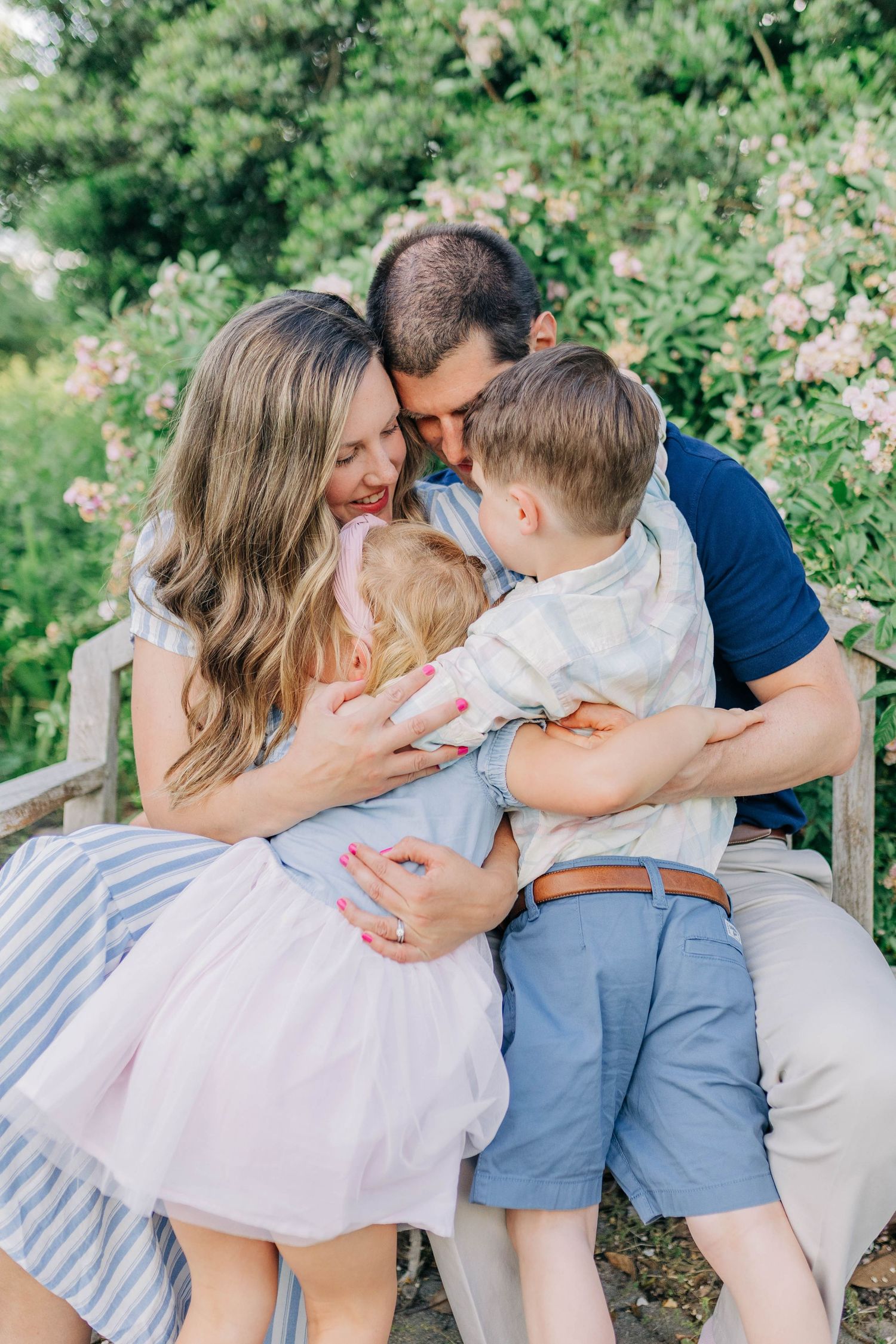 A joyful family embraces while sitting on a wooden bench in a lush garden setting.