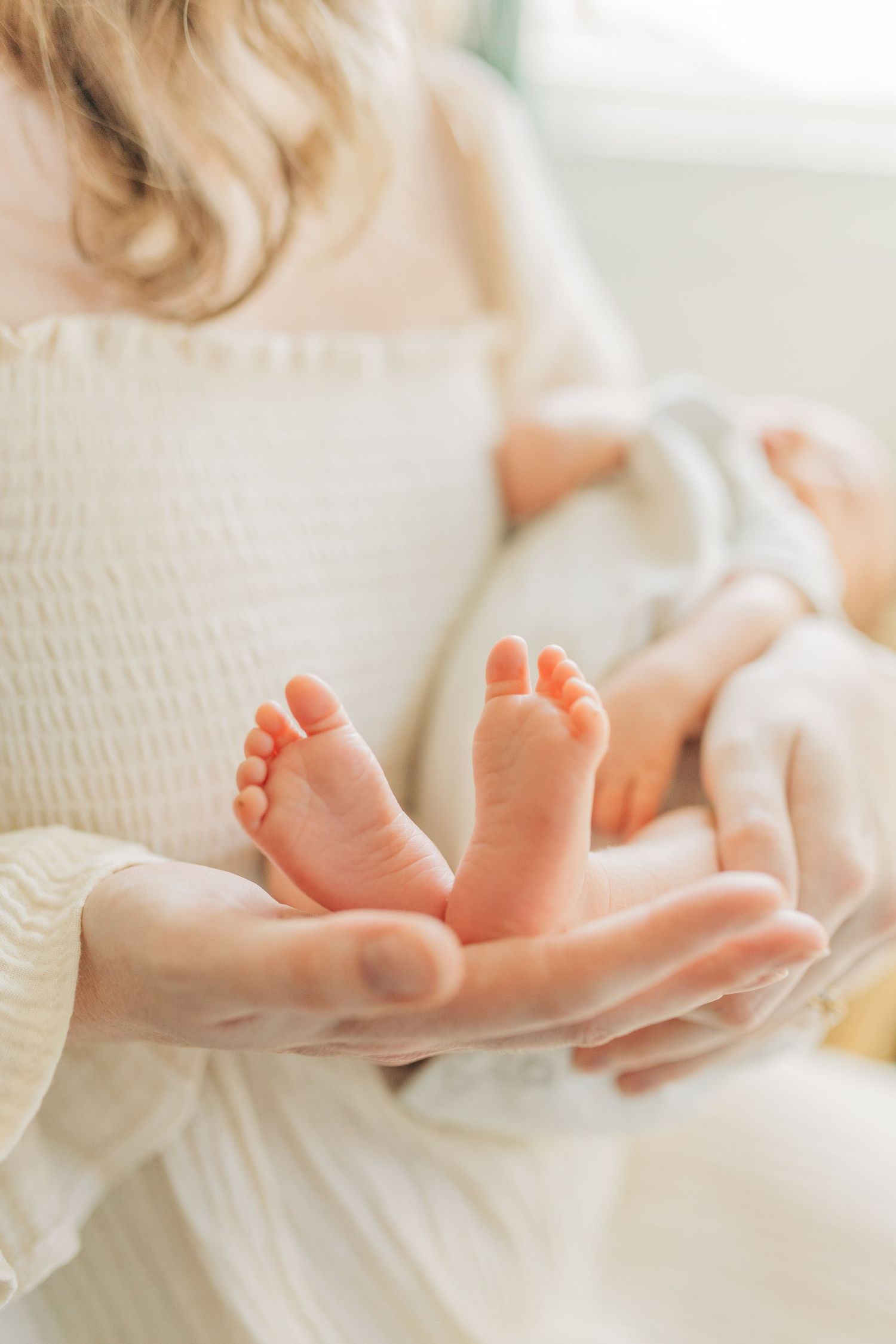 Tiny newborn baby feet being gently cradled in adult hands against white fabric background.
