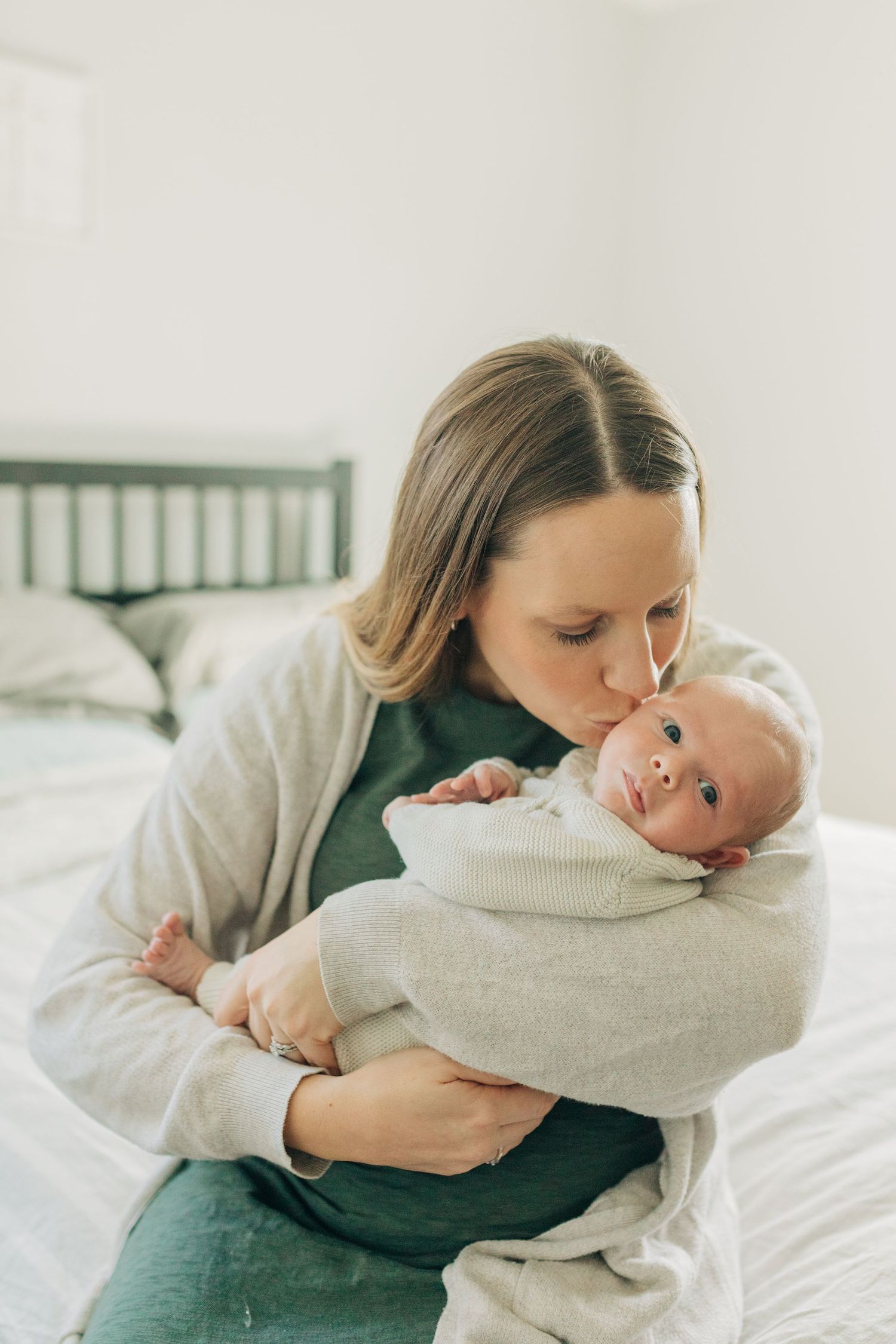 A tender moment between parent and newborn baby wrapped in cream colored blanket on white bedding.