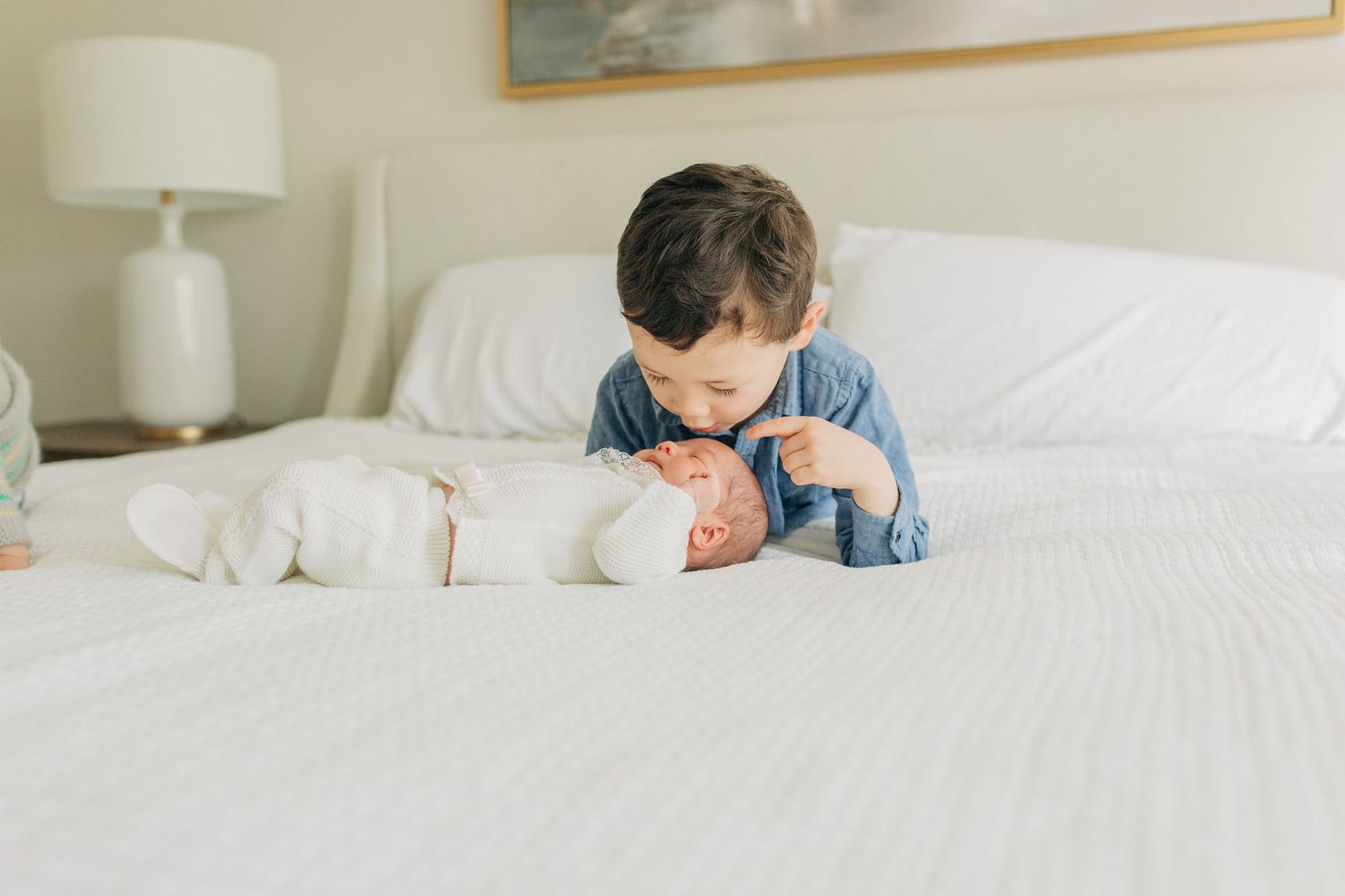 Children relaxing on white bedding in a bright bedroom with decorative wall art.