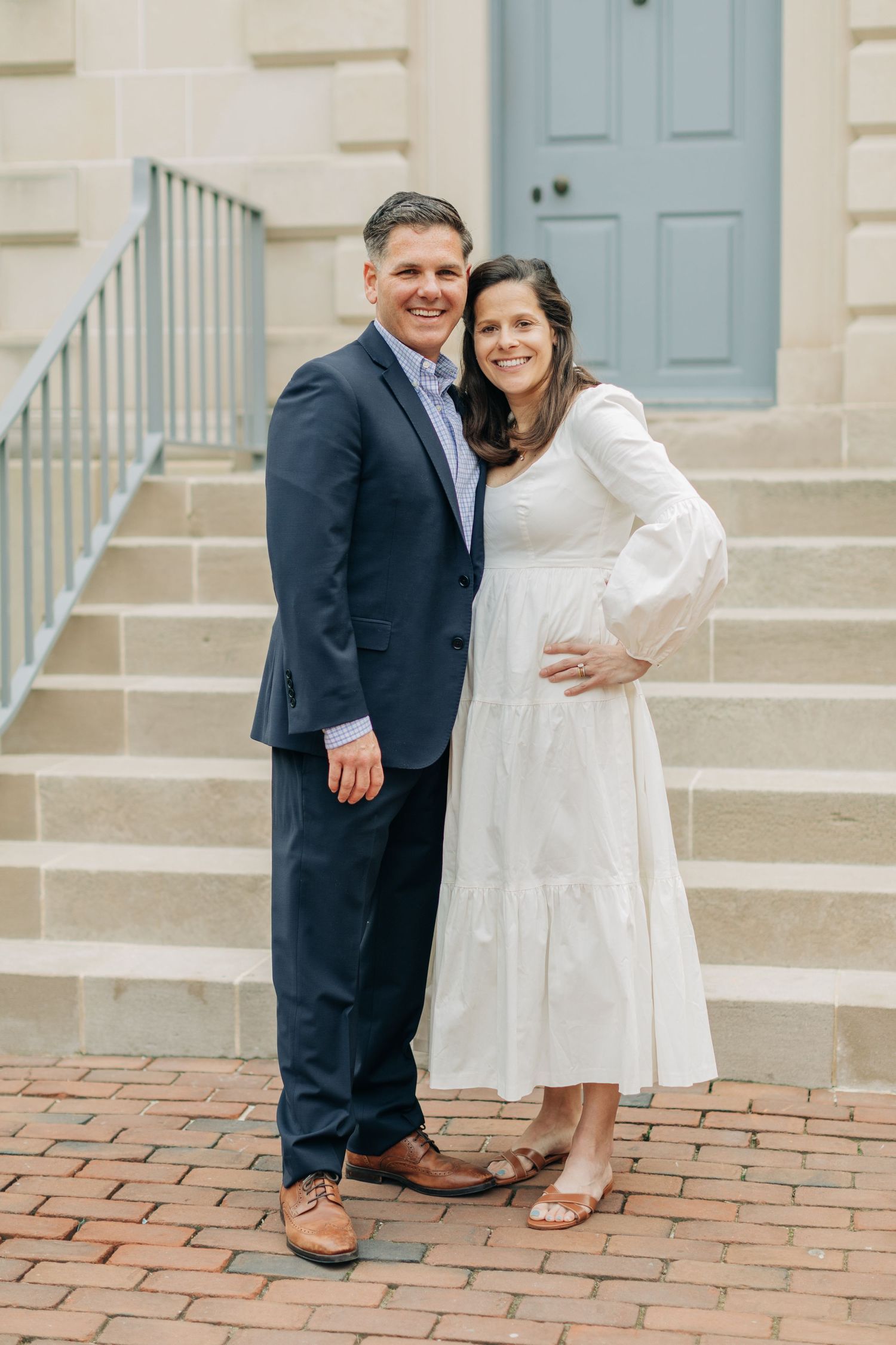 Couple poses on brick steps with blue door in background.
