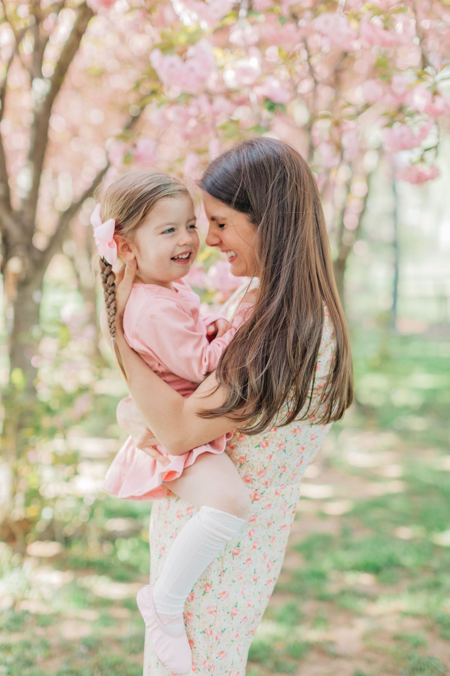 Playful interaction between parent and child during springtime cherry blossom photo session.