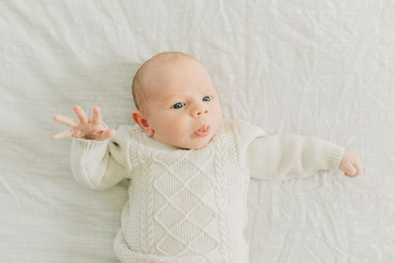 Baby in textured white sweater resting on light colored surface.