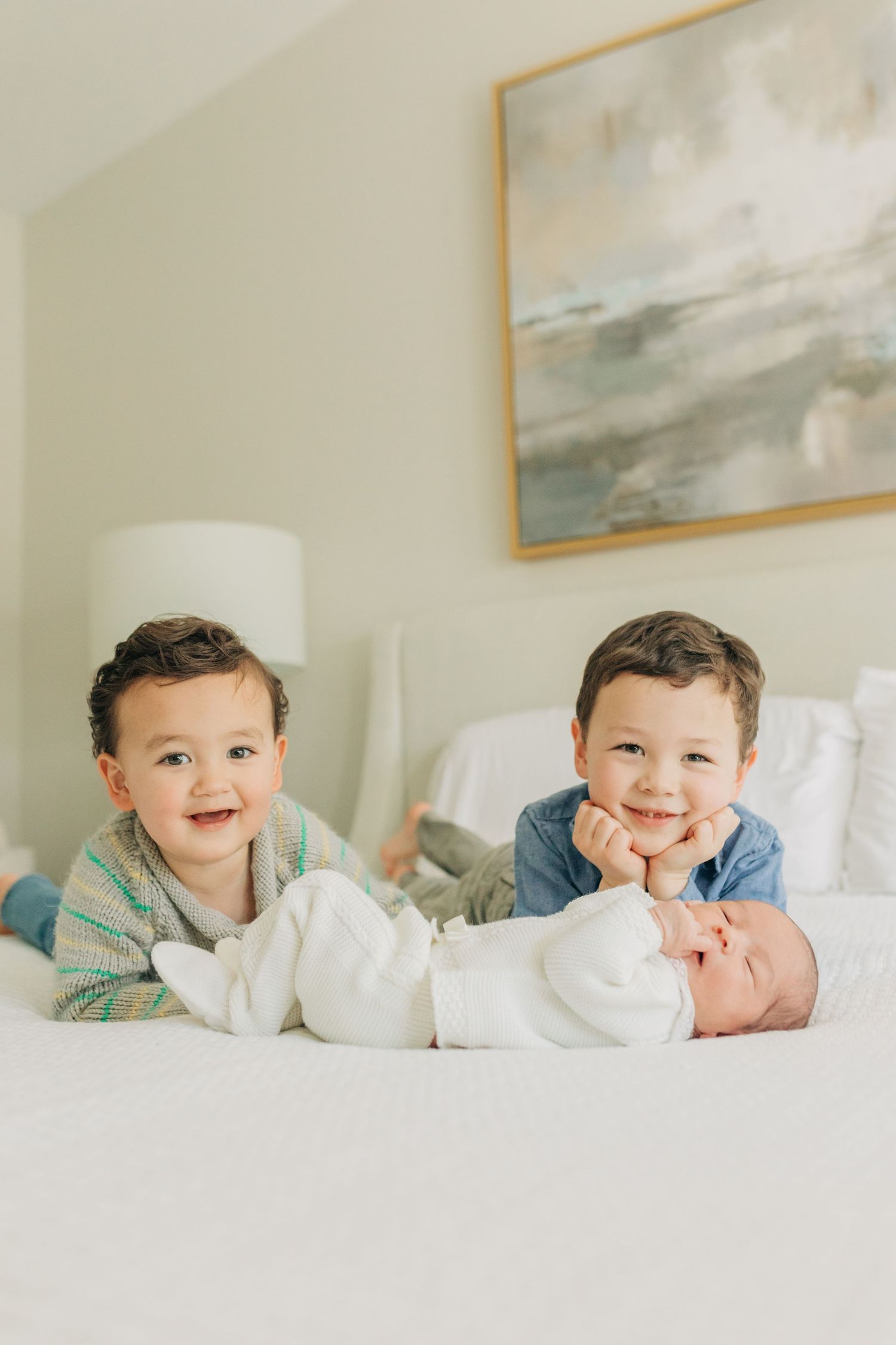 Children posing on white bedding with joyful smiles in a light-filled bedroom.