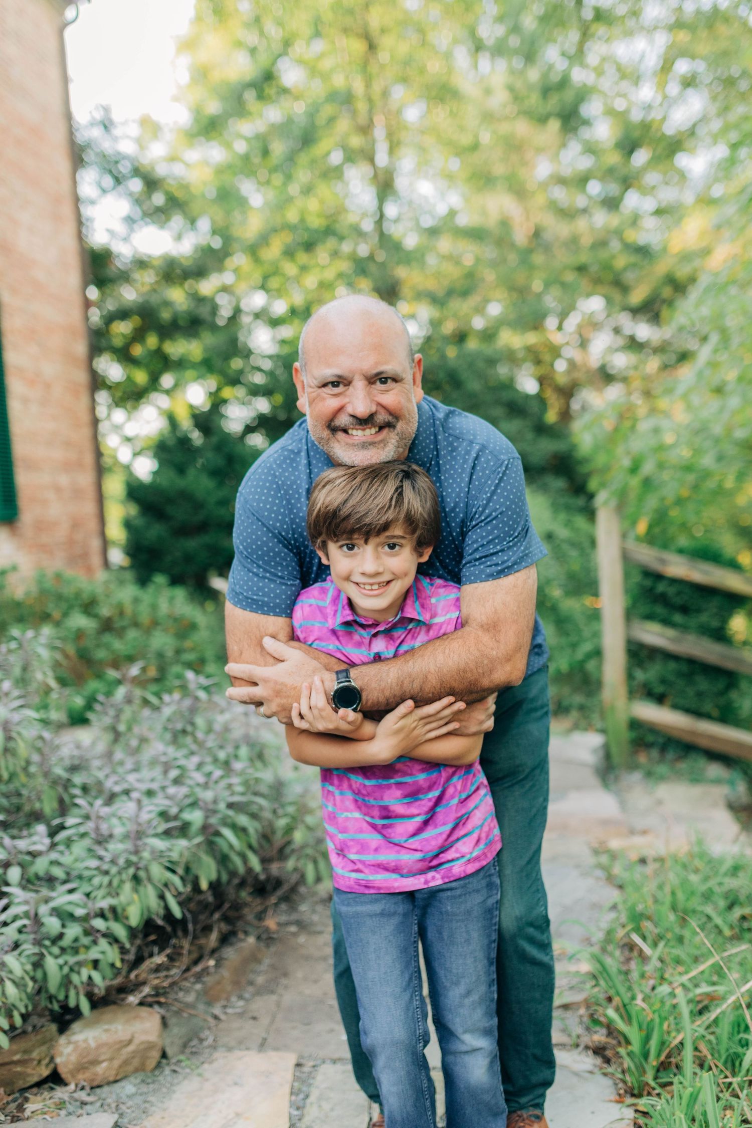 Playful outdoor portrait session with joyful embraces against a backdrop of brick and greenery.