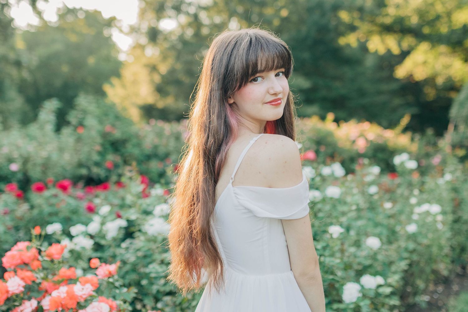 Dreamy garden portrait with someone in an off-shoulder white dress among blooming flowers.