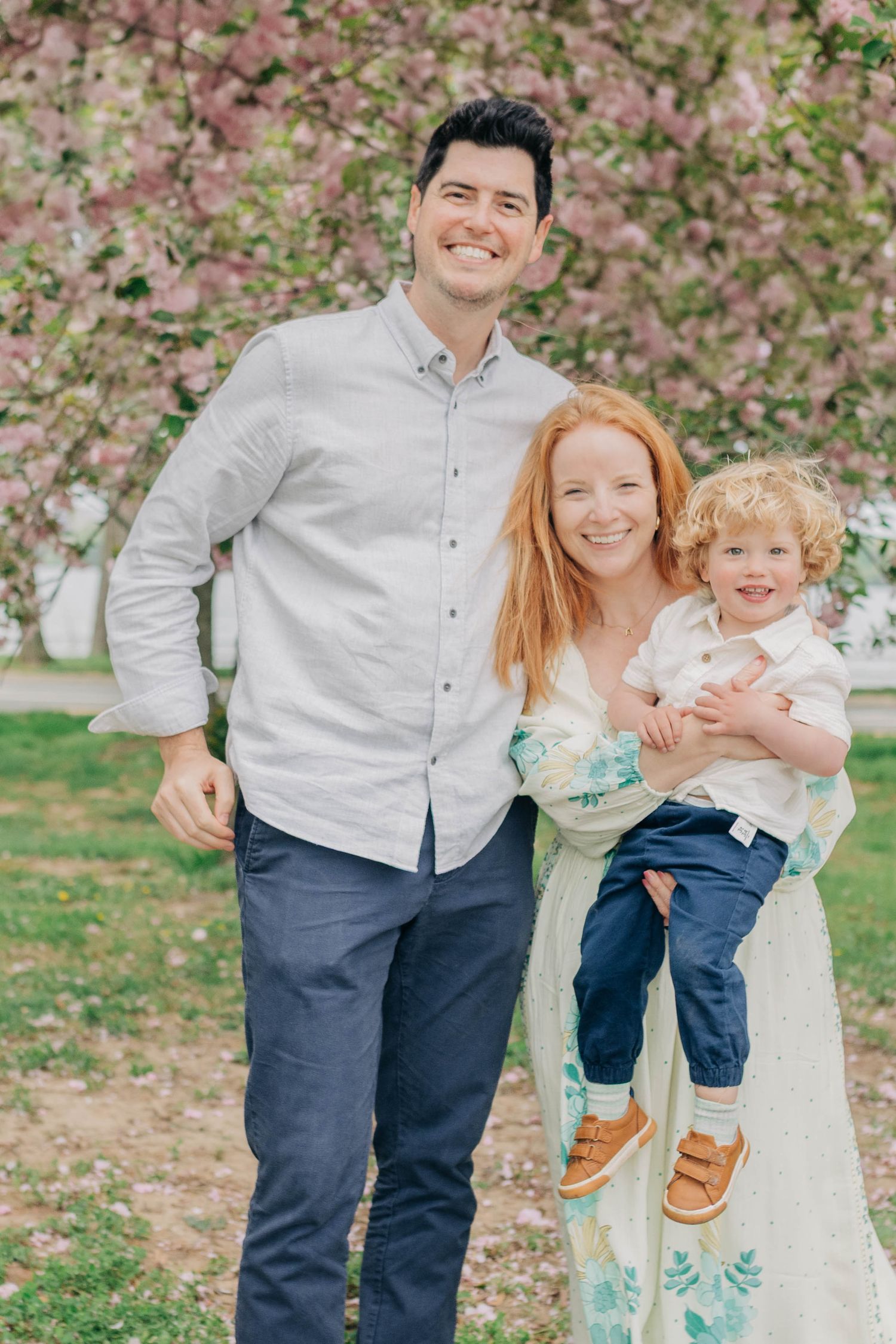 A family shares joyful moments together in a park with blooming cherry blossoms in the background.