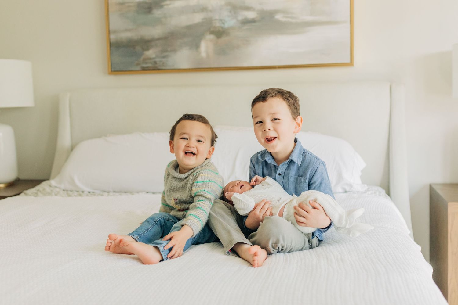 Children share joyful moments while lying together on a white bed.