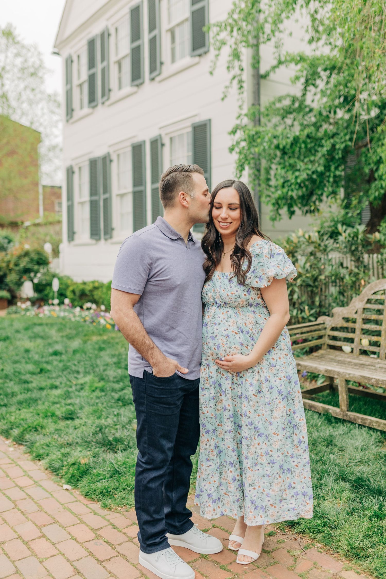 A couple laughs together during their maternity photoshoot in a garden setting.